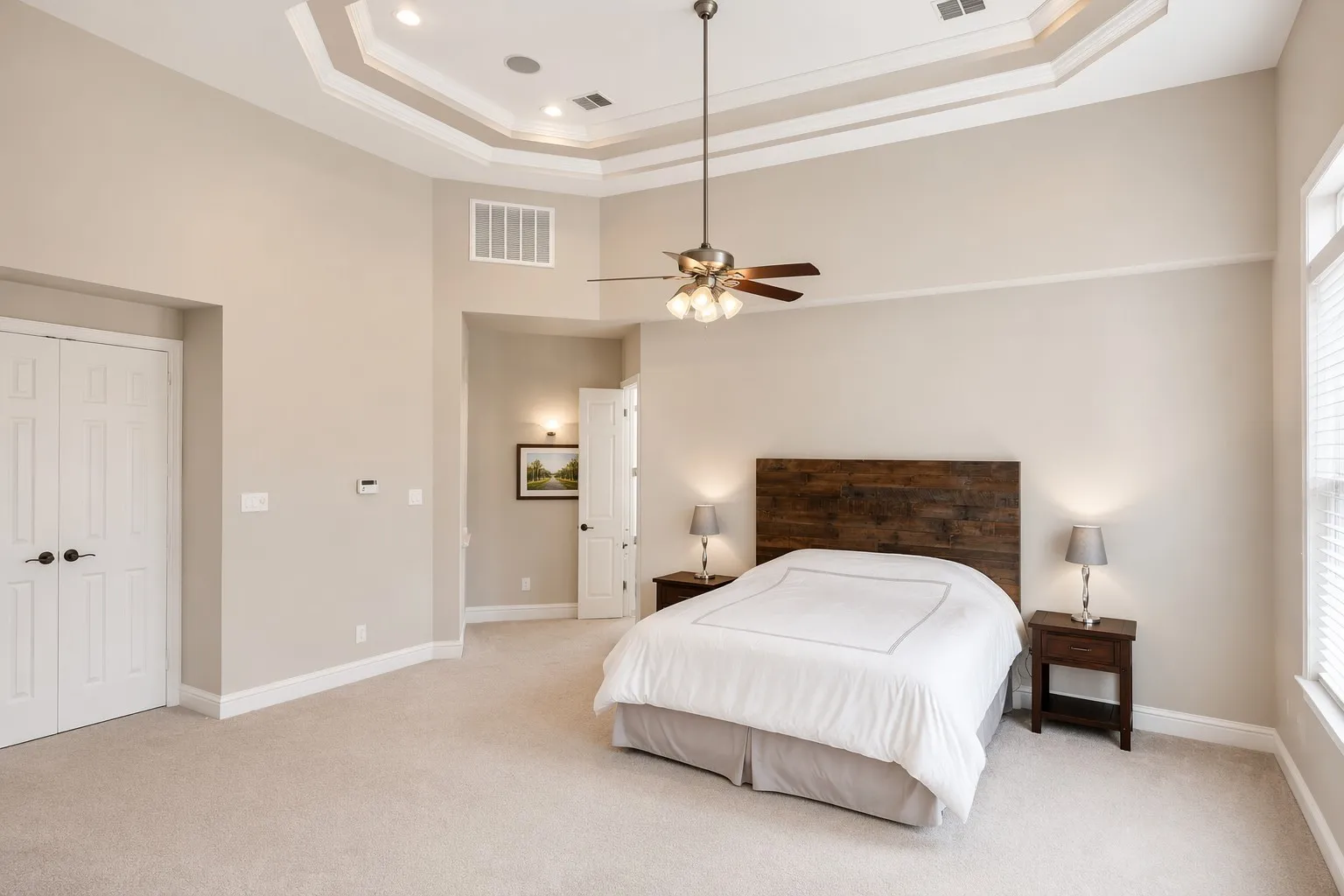 Spacious room featuring a multi-tiered tray ceiling with recessed lighting, light neutral-toned carpeting, and a ceiling fan