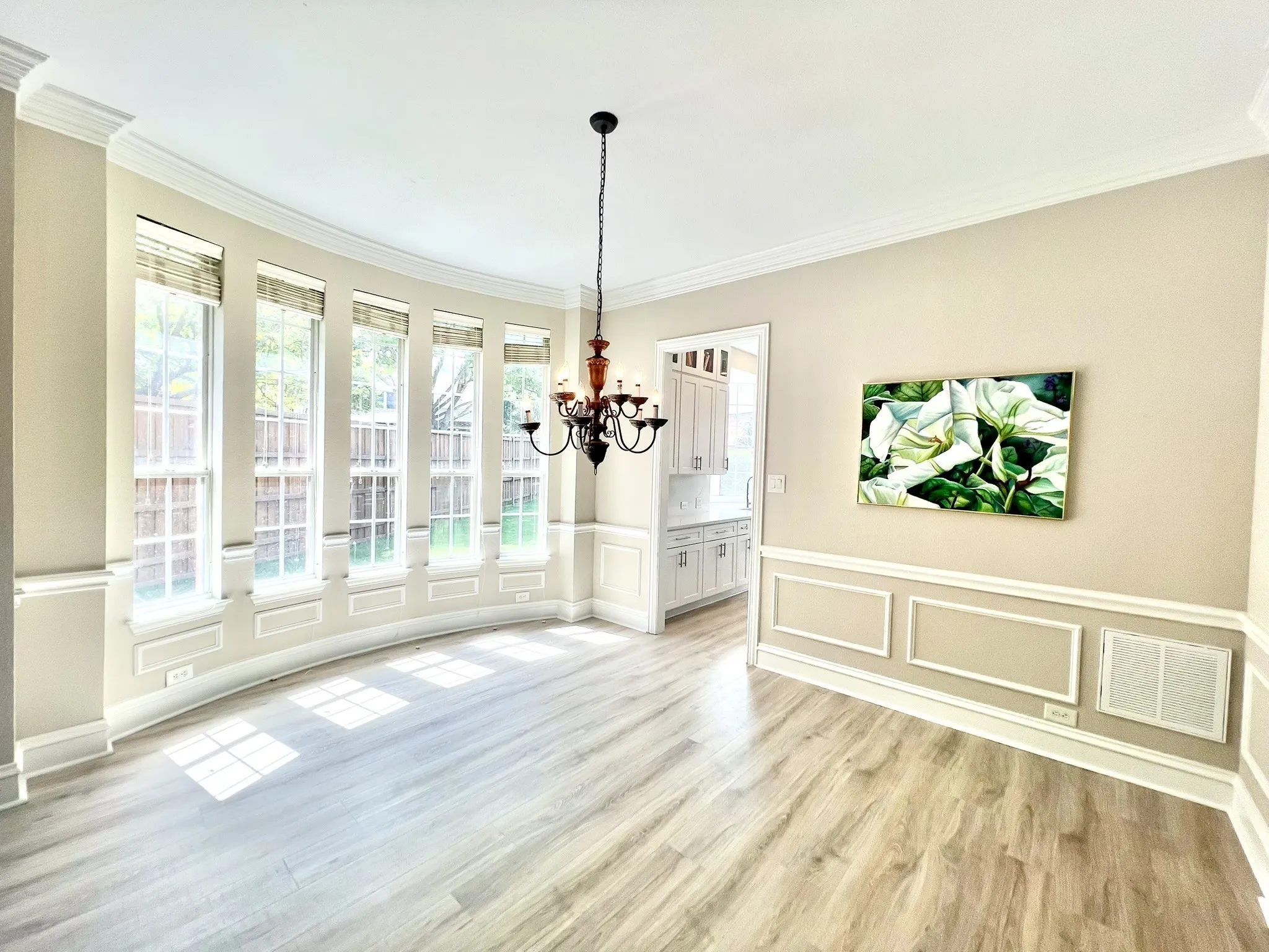 Curved bay window wall with five multi-pane windows, crown molding, chair rail molding, and light wood-finish flooring