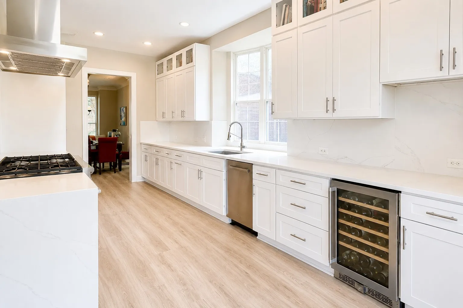 Kitchen featuring light wood-finish flooring, white cabinetry, integrated stainless steel appliances, a gas range with an overhead vent hood, and solid surface countertops