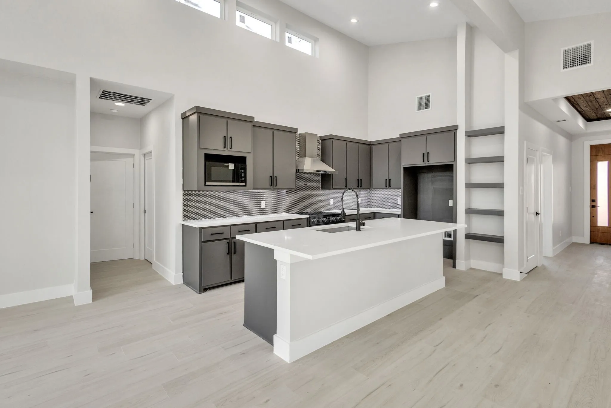 Kitchen with black microwave, gray cabinets, a kitchen island with sink, and wall chimney range hood