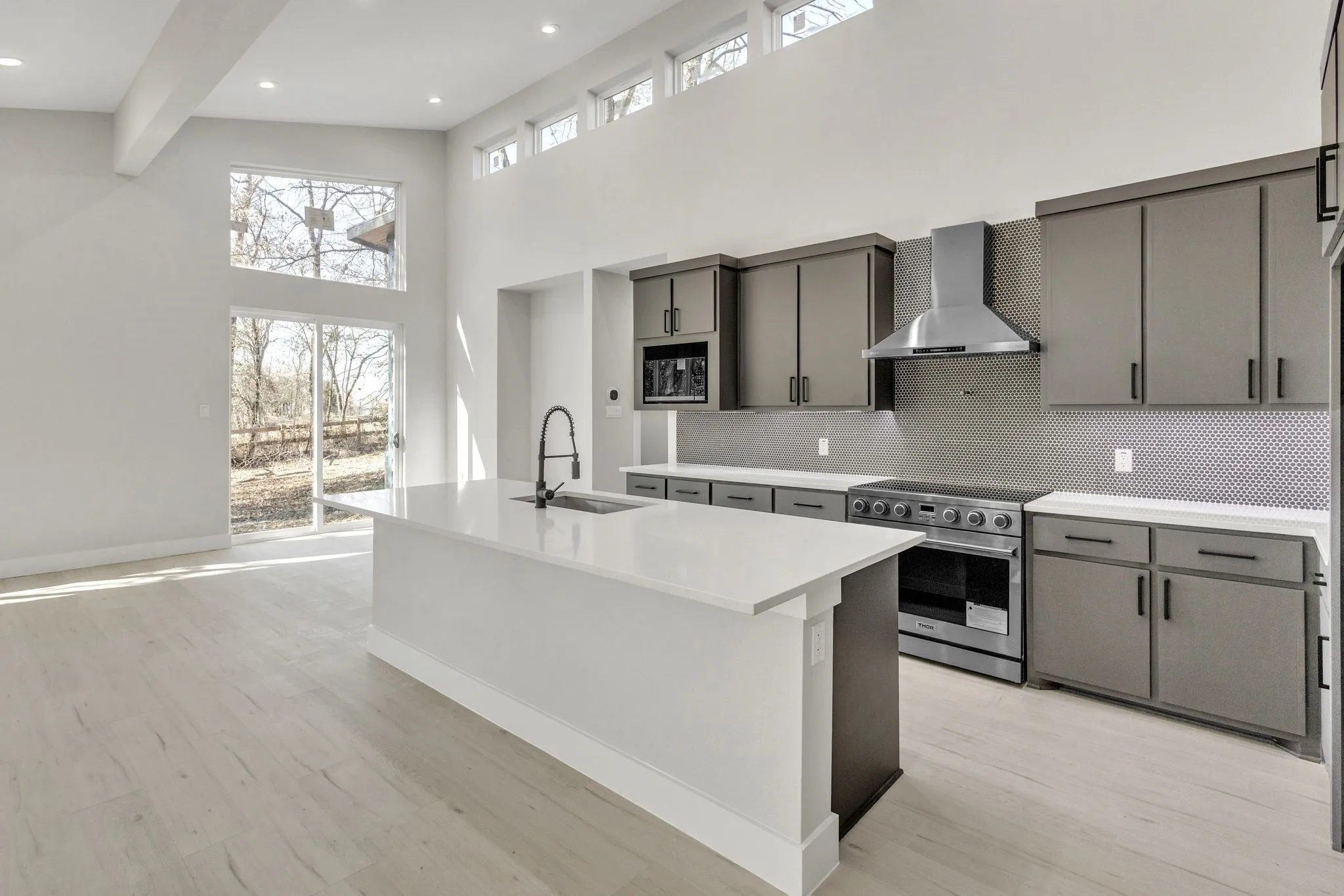 Kitchen featuring sink, gray cabinetry, stainless steel range with electric cooktop, wall chimney range hood, and an island with sink