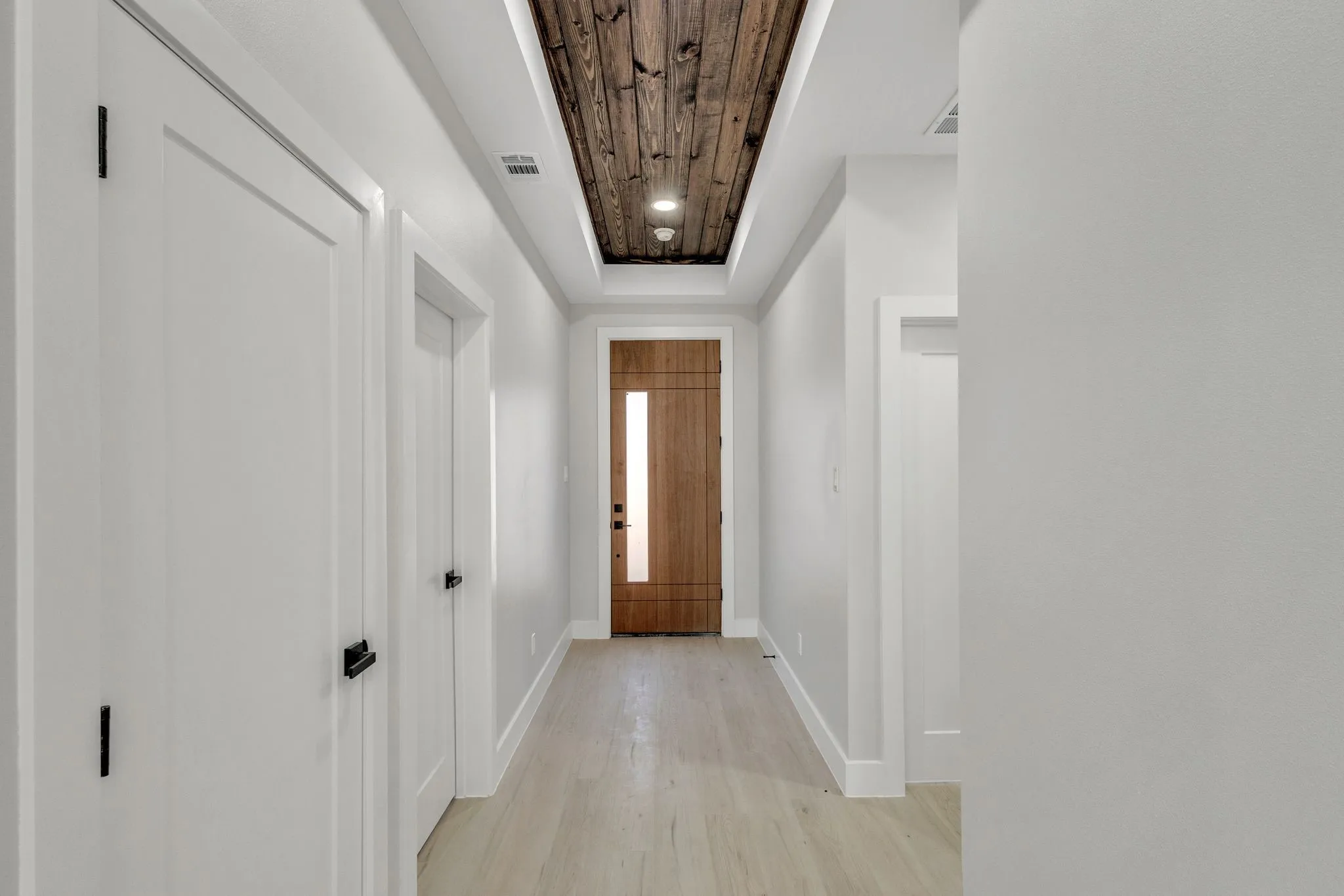 Doorway to outside featuring wood ceiling, light wood-type flooring, and a tray ceiling