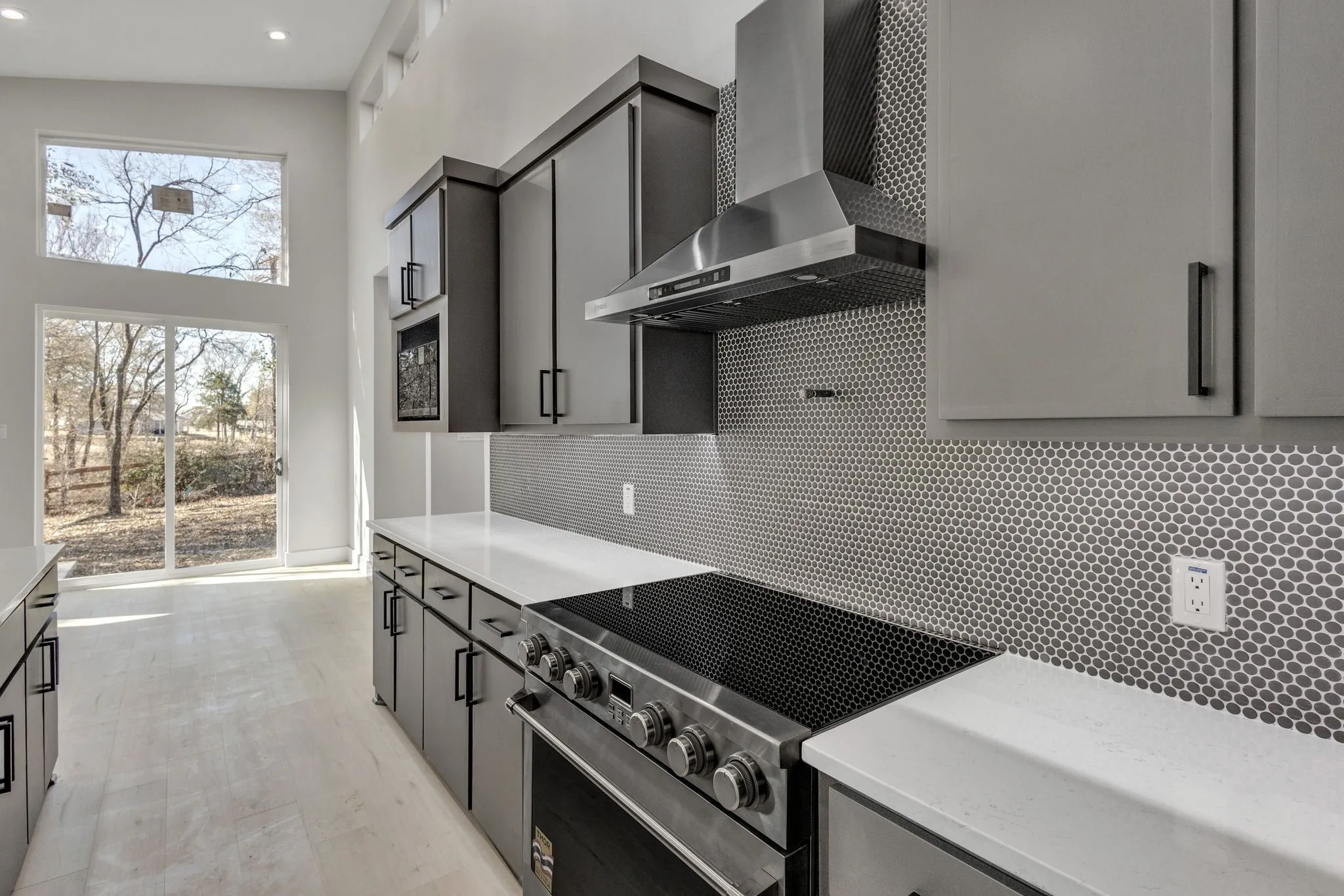 Kitchen with a towering ceiling, tasteful backsplash, stainless steel electric range oven, wall chimney range hood, and gray cabinets