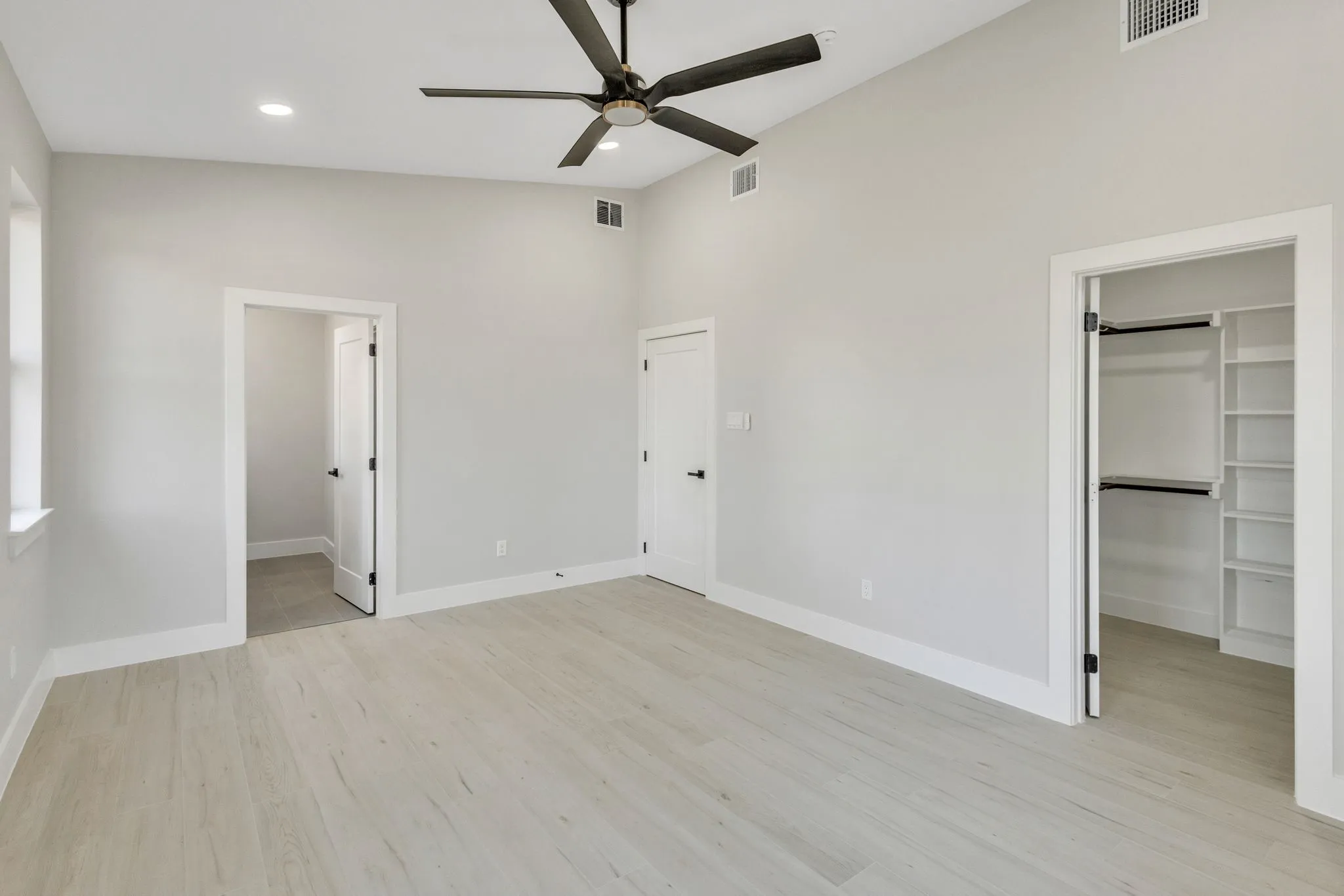 Unfurnished bedroom featuring a walk in closet, light wood-type flooring, a closet, ceiling fan, and connected bathroom