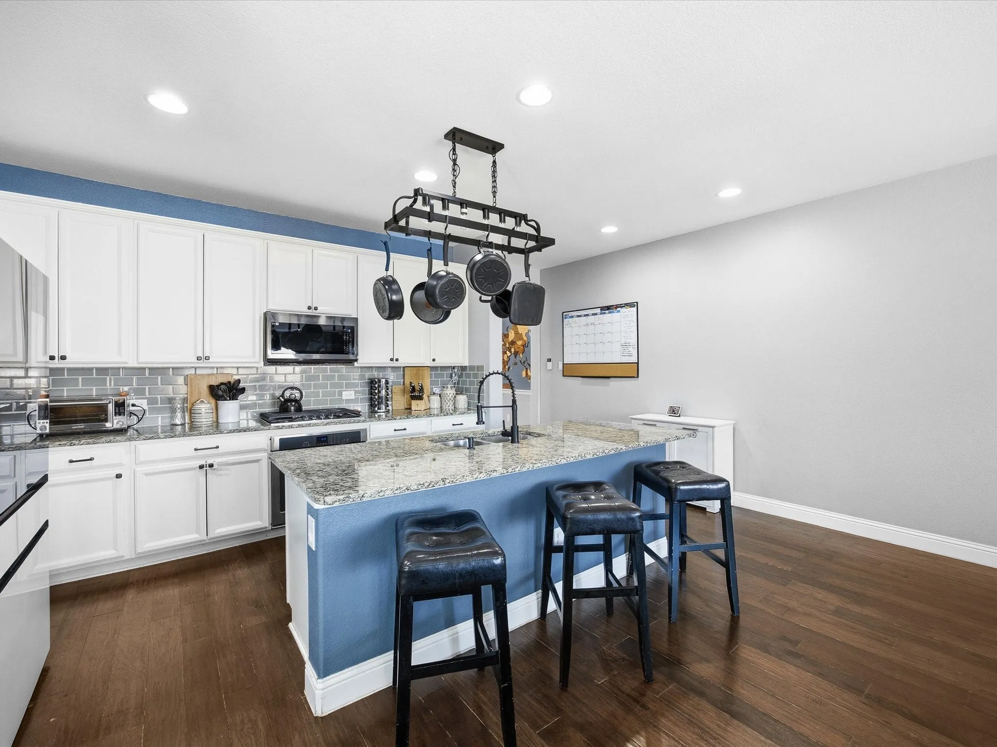 Kitchen featuring a breakfast bar area, white cabinets, light stone countertops, an island with sink, and recessed lighting