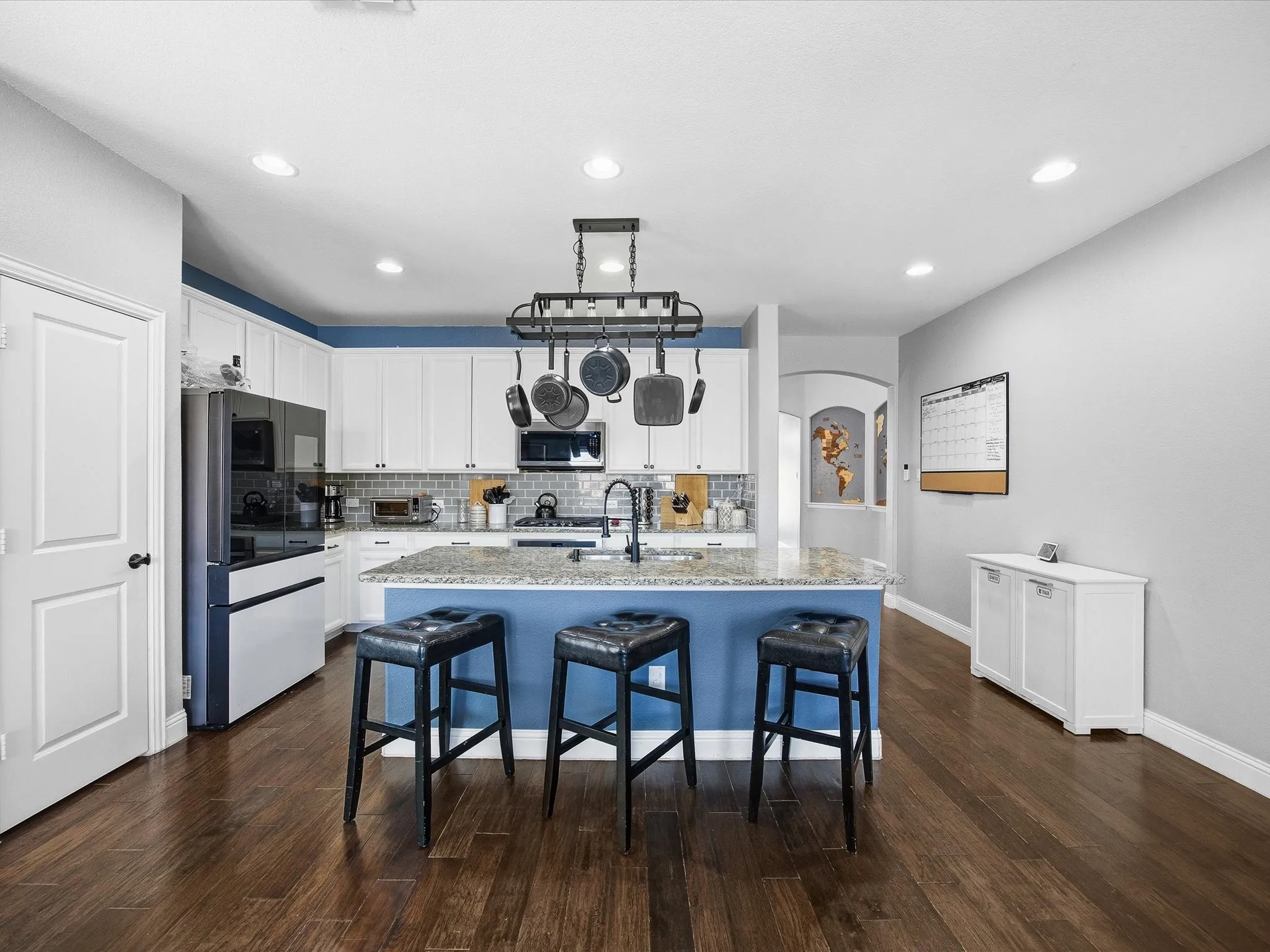 Kitchen with smart refrigerator, a kitchen breakfast bar, a kitchen island with sink, white cabinets, and arched walkways
