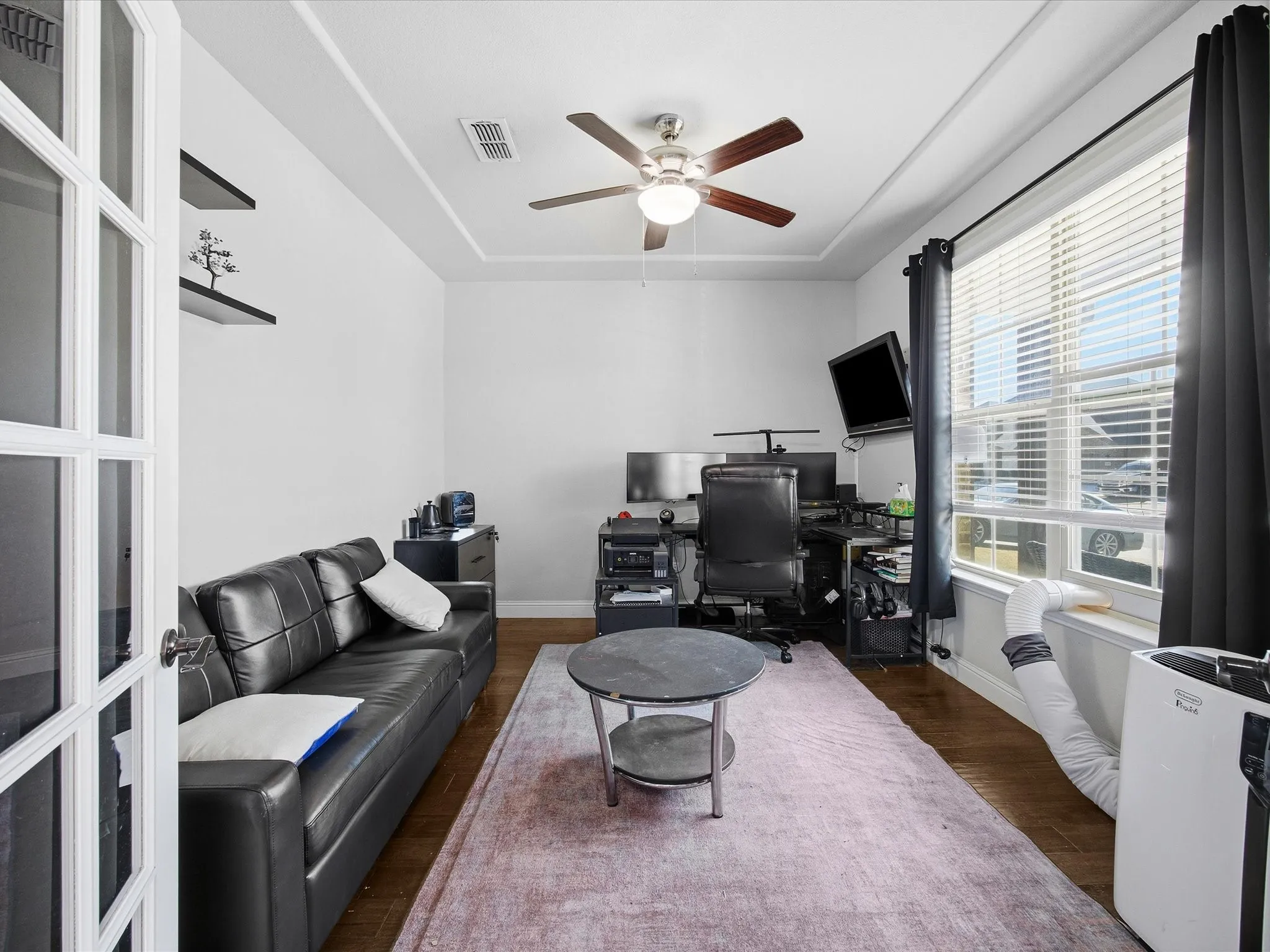 Home office with a raised ceiling, dark wood-type flooring, and ceiling fan
