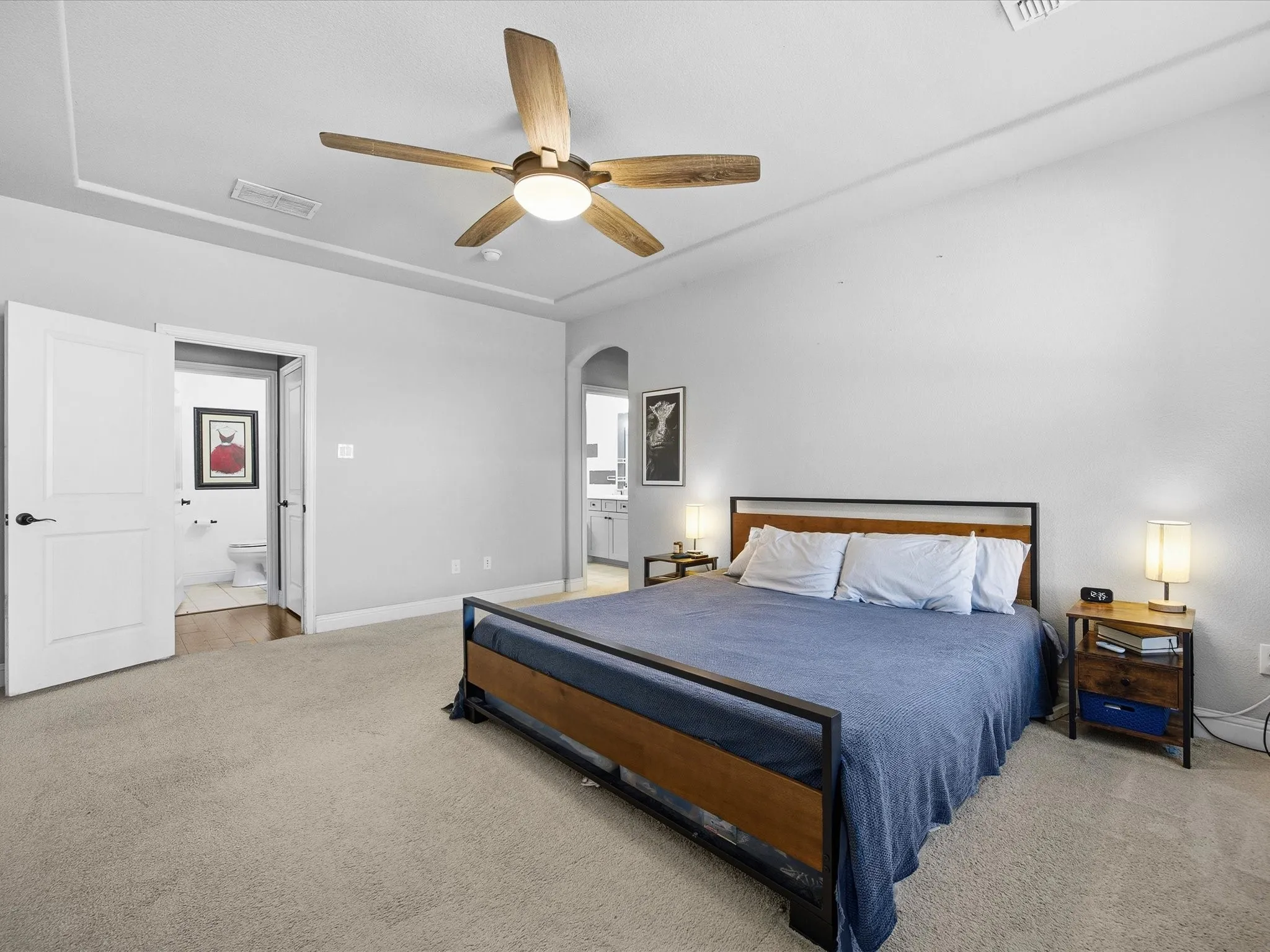 Primary Bedroom featuring light carpet, arched walkways, ensuite bath, and ceiling fan