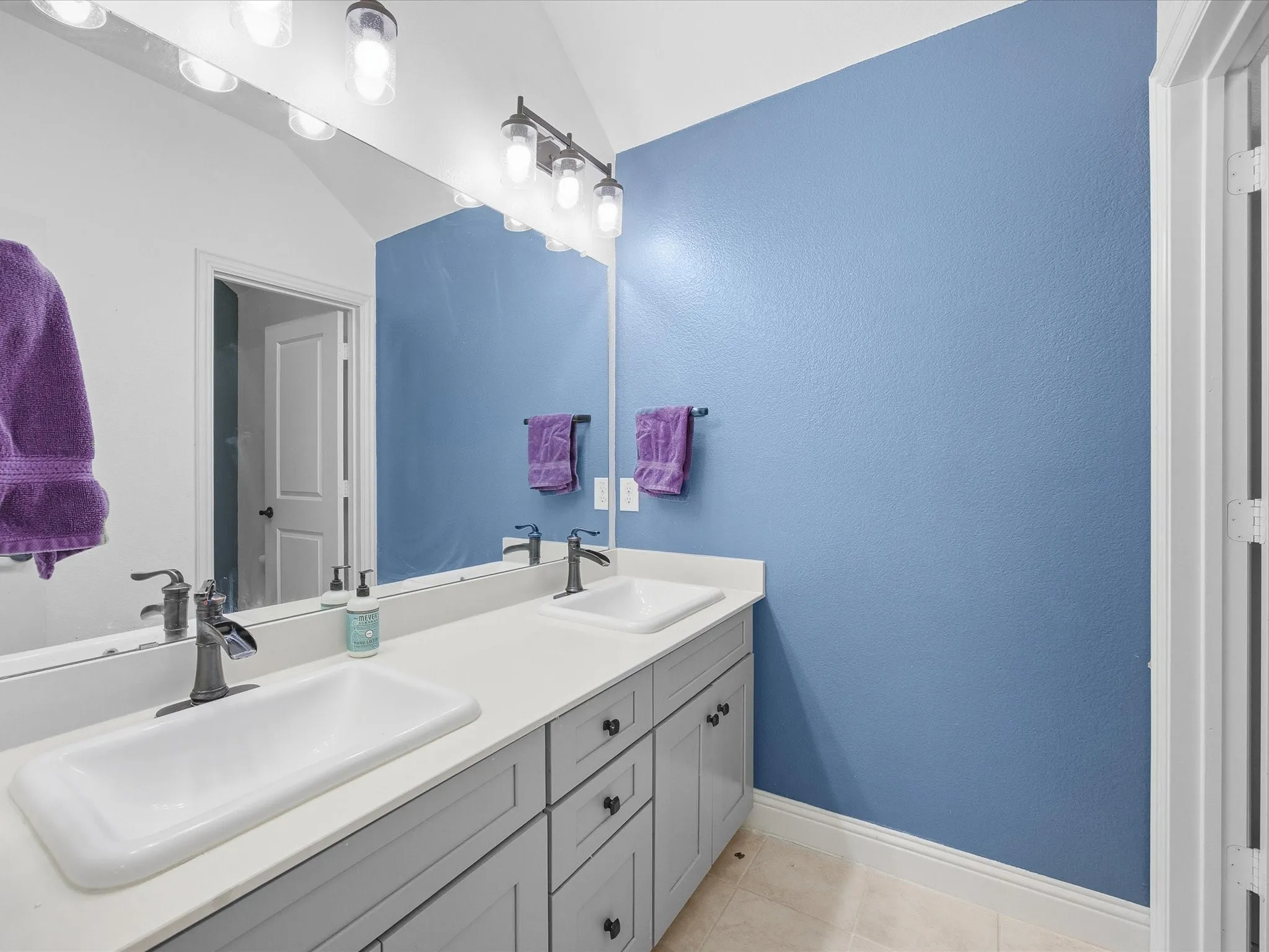 Full bathroom featuring double vanity, light tile patterned floors, lofted ceiling, and a textured wall