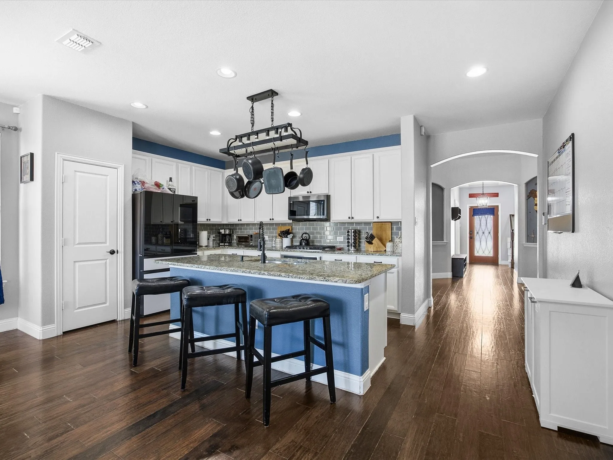 Kitchen featuring arched walkways, a kitchen island with sink, white cabinetry, a kitchen breakfast bar, and dark wood-type flooring