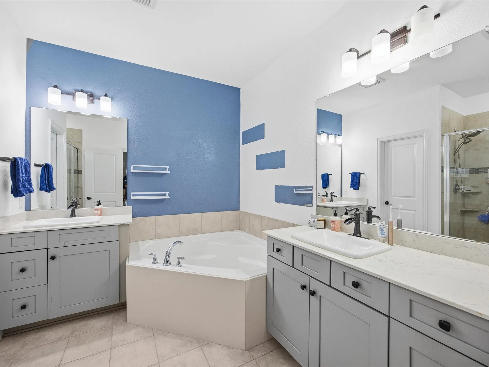 Primary Bathroom featuring a stall shower, two vanities, a bath, and light tile patterned floors
