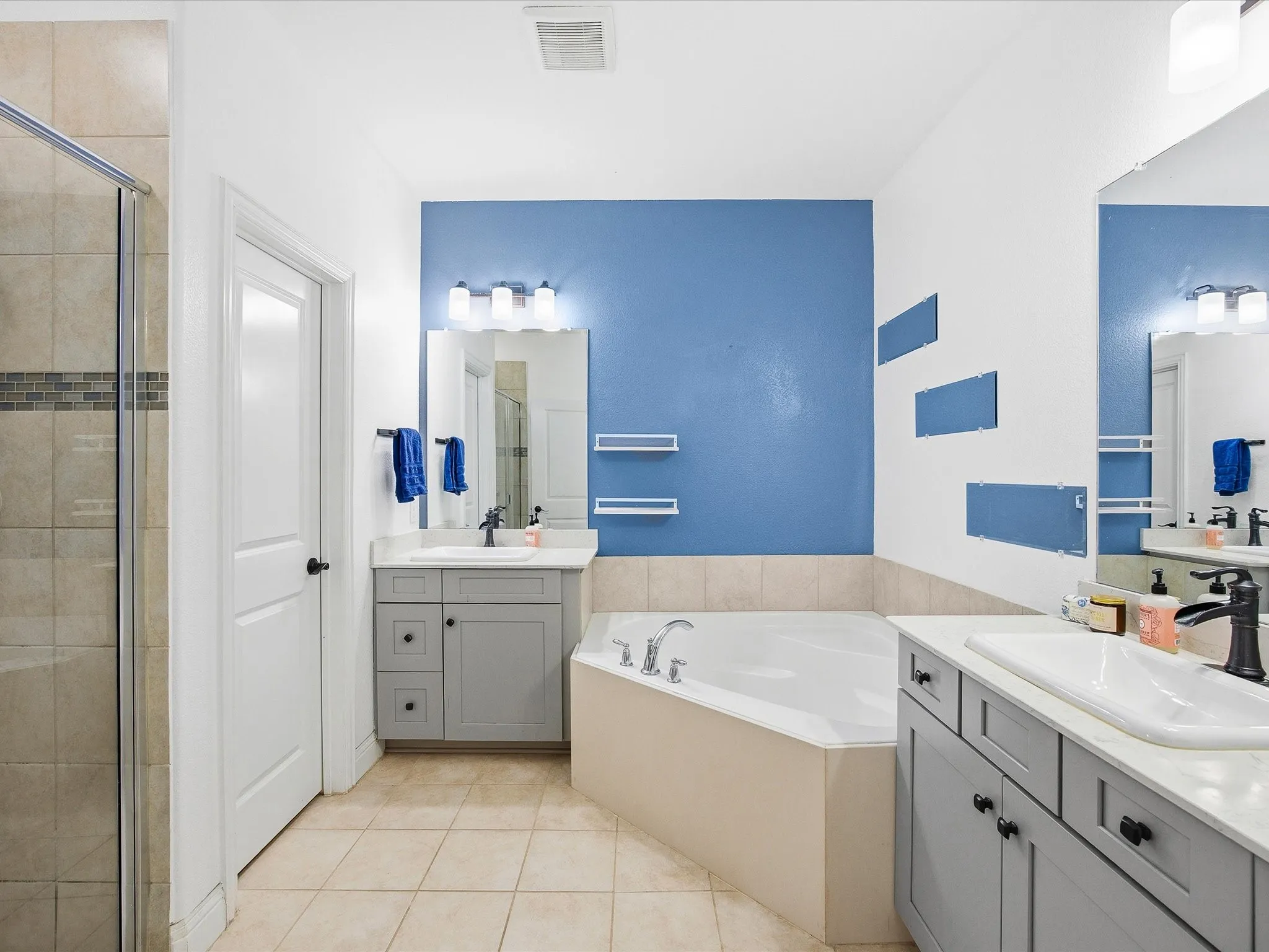 Primary Bathroom featuring a shower stall, a garden tub, two vanities, and light tile patterned floors