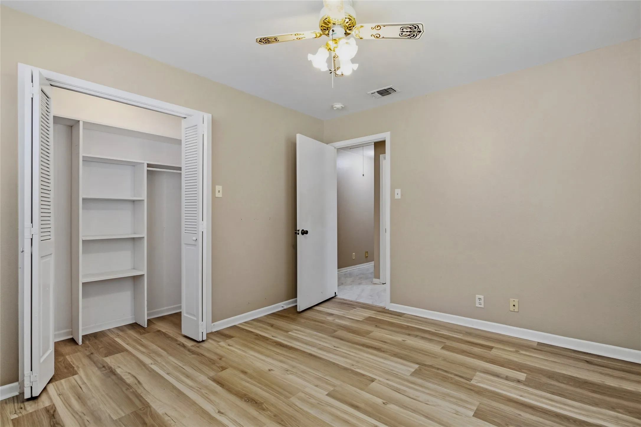 Wood-finish flooring, built-in closet shelving, bifold closet doors, ceiling fan with light fixture, and neutral wall tones