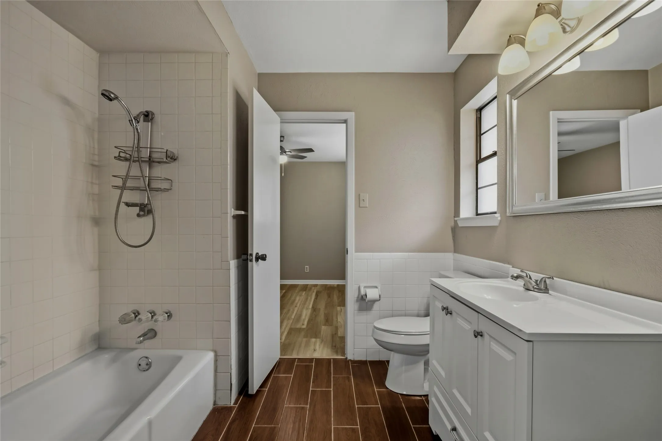 White tile bath surround, white porcelain bathtub, and white vanity with an integrated sink