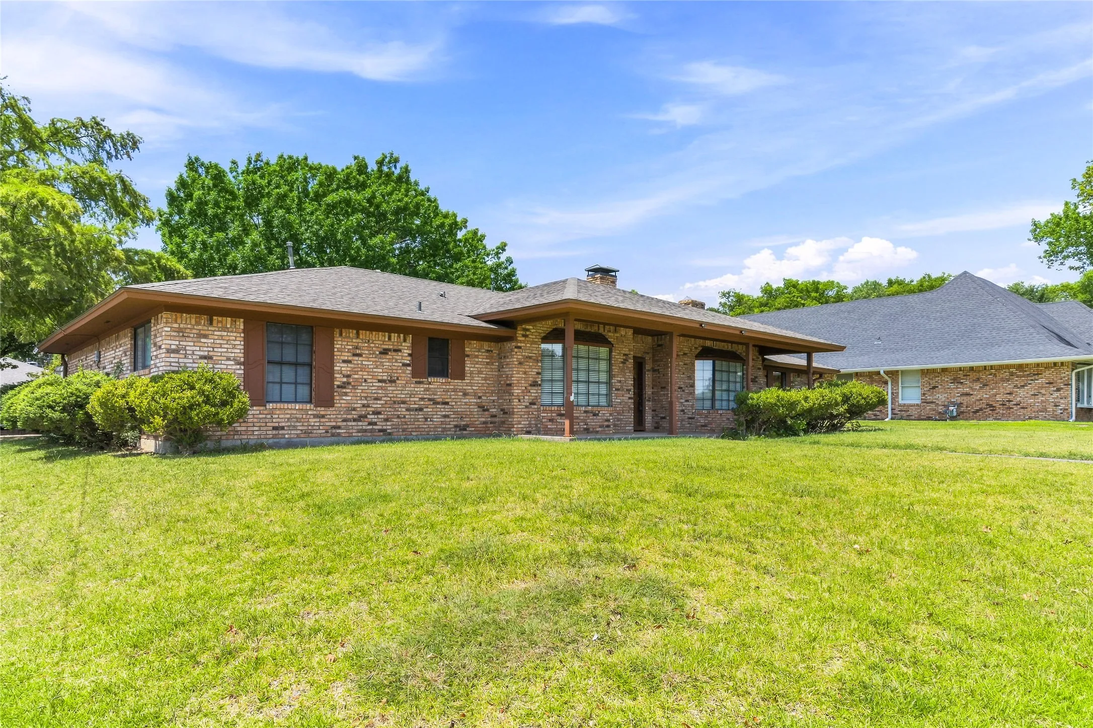 Brick exterior with a covered porch entry, multiple windows, and a shingle roof