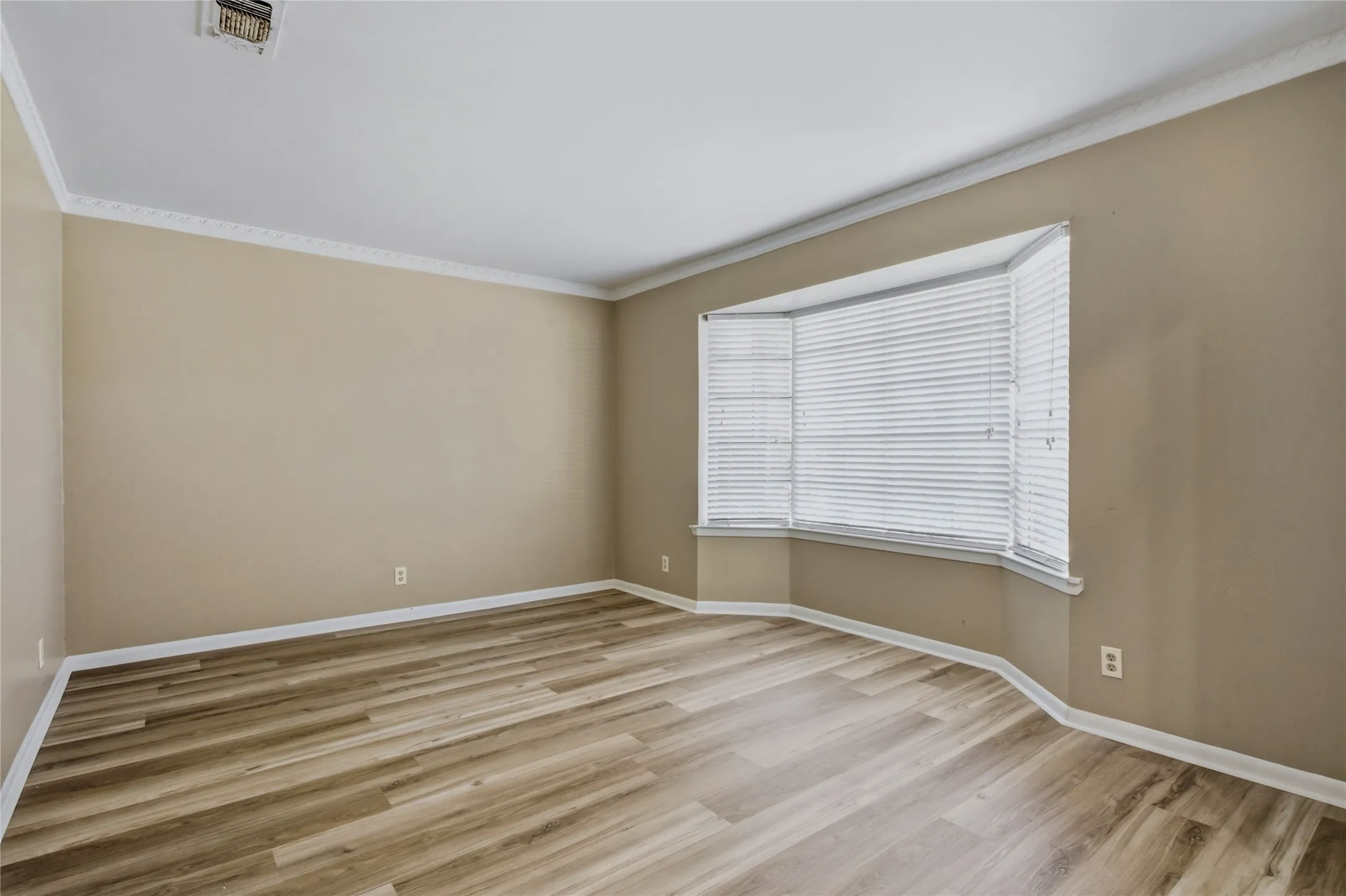 Expansive room featuring wood-finish flooring, neutral-toned walls, and white crown molding