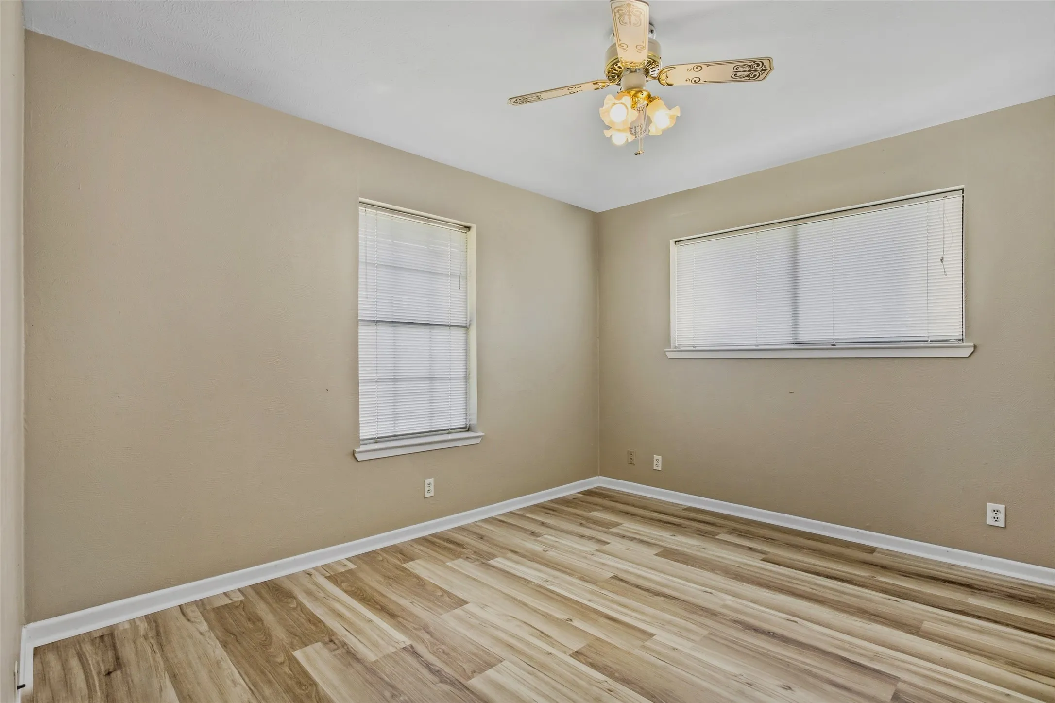 Wood-finish flooring, two windows with blinds, ceiling fan with integrated lighting, and neutral wall tones