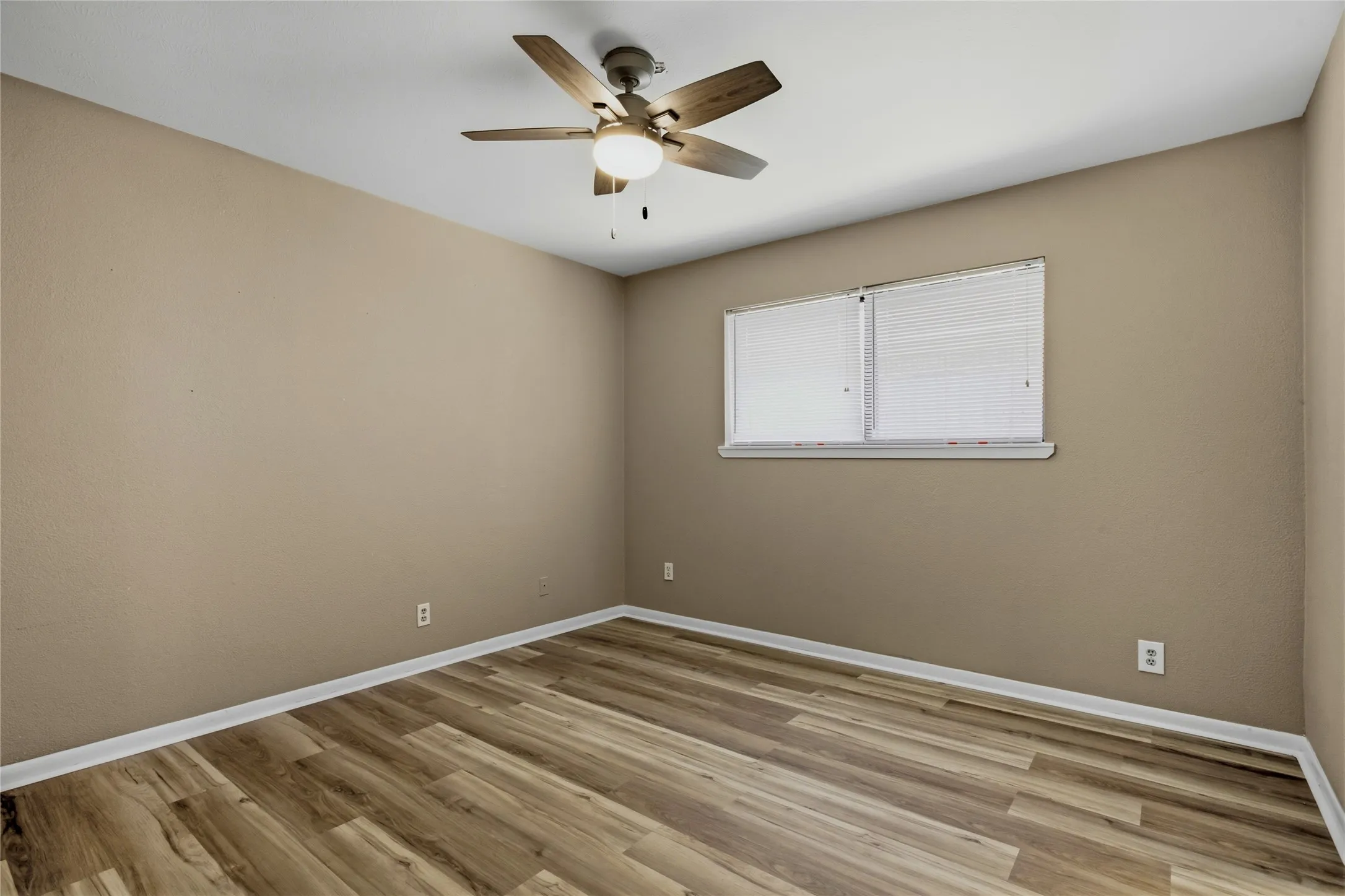 Neutral tone walls, wood-finish flooring, white trim, ceiling fan with integrated lighting, and a double window with blinds