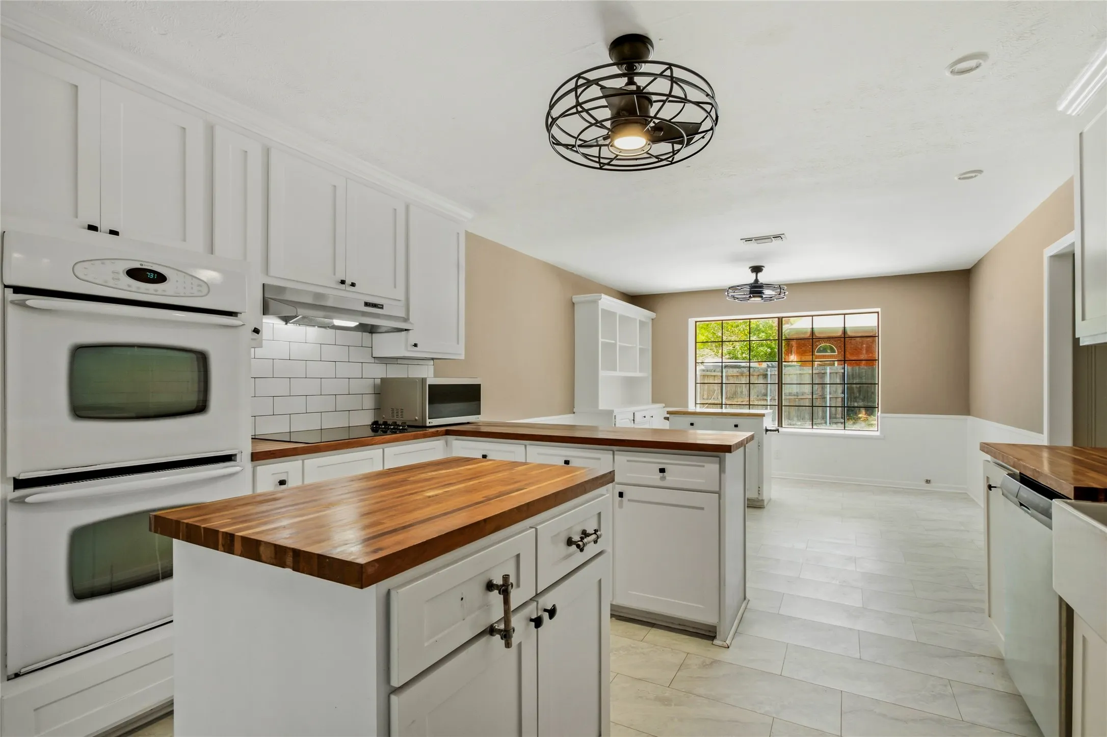 Spacious kitchen featuring white cabinetry, wood-finish countertops, subway tile backsplash, and built-in double ovens