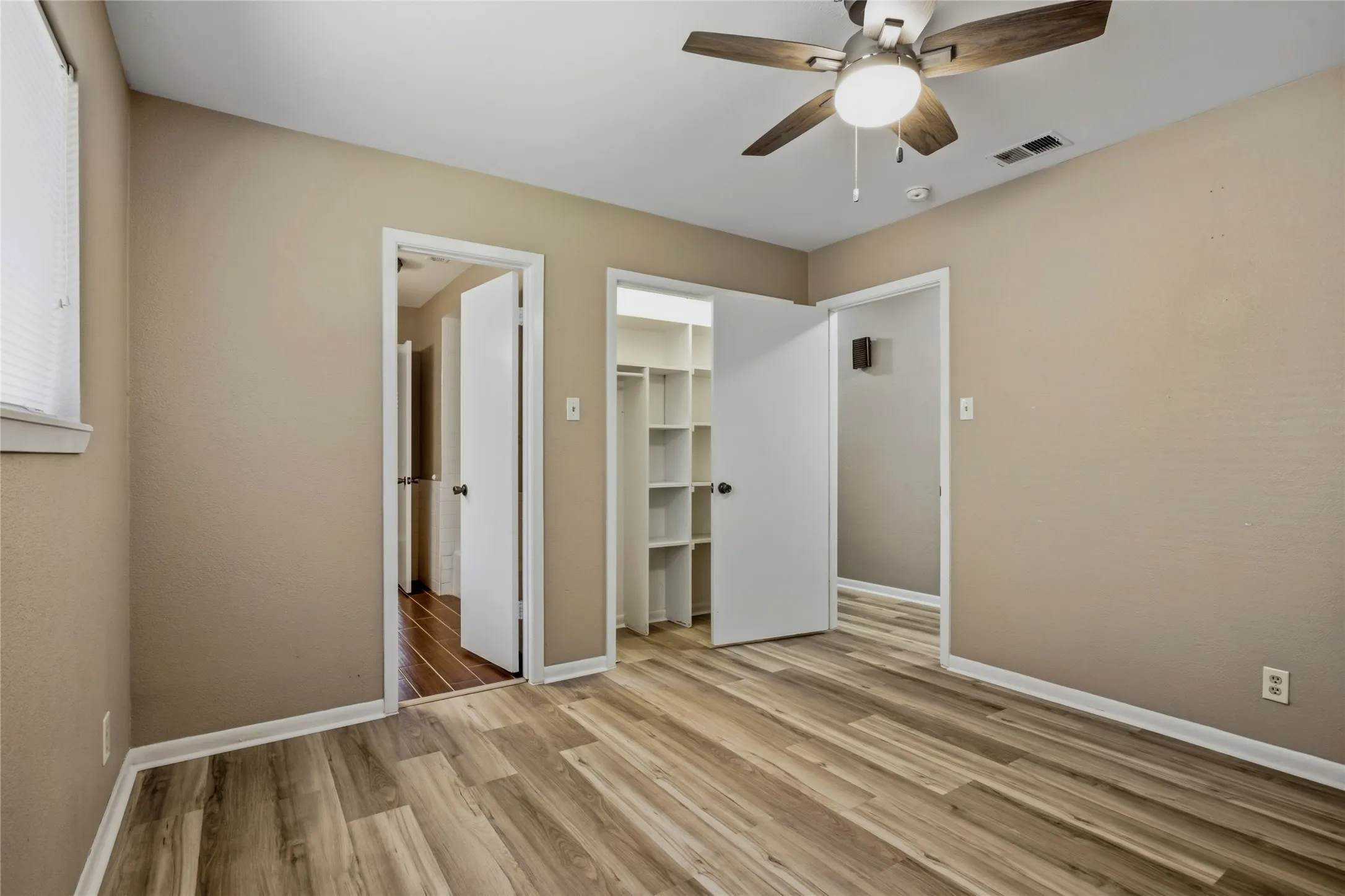 Wood-finish flooring, ceiling fan with integrated lighting, window with blinds, and a built-in closet system