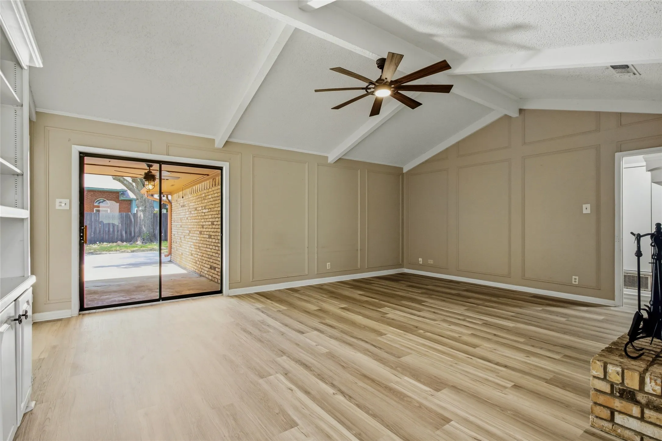 Vaulted ceiling with exposed beams, wood-finish flooring, sliding glass patio door, built-in shelving, and wood panel wall accents