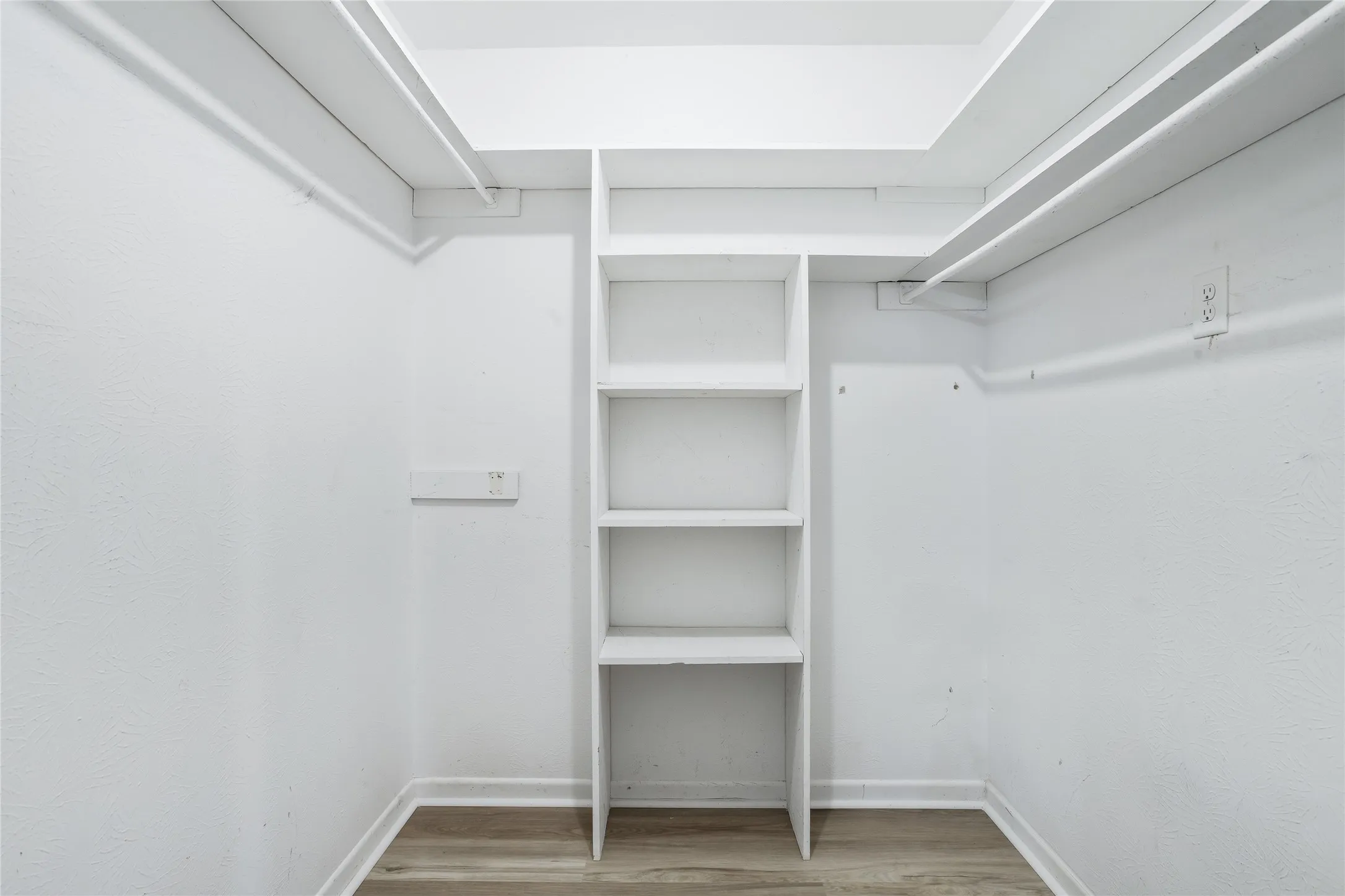 Built-in shelving unit, white walls, wood-finish flooring, and upper storage shelves