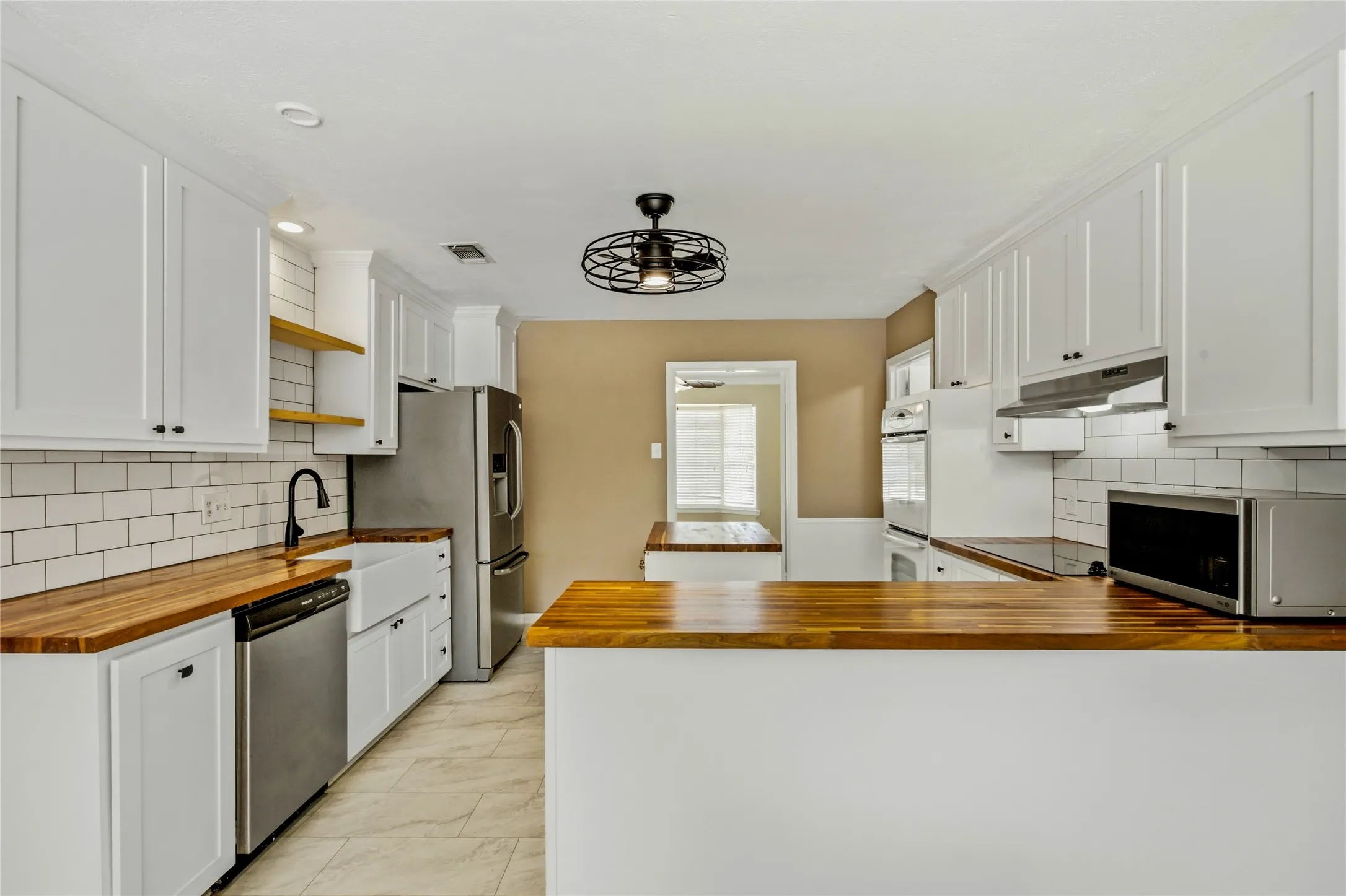 White cabinetry, wood-finish countertops, subway tile backsplash, stainless steel appliances, and a farmhouse sink