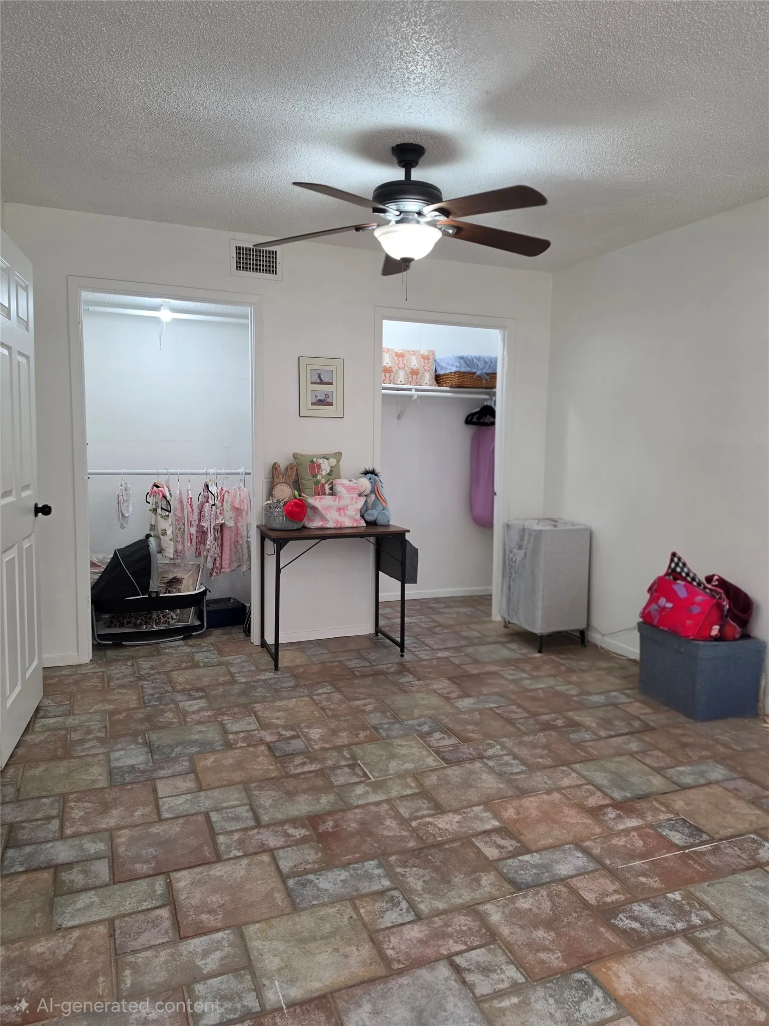 Spacious room featuring multi-toned tile flooring, two open closet spaces with shelving, a white paneled door, and a ceiling fan with integrated lighting
