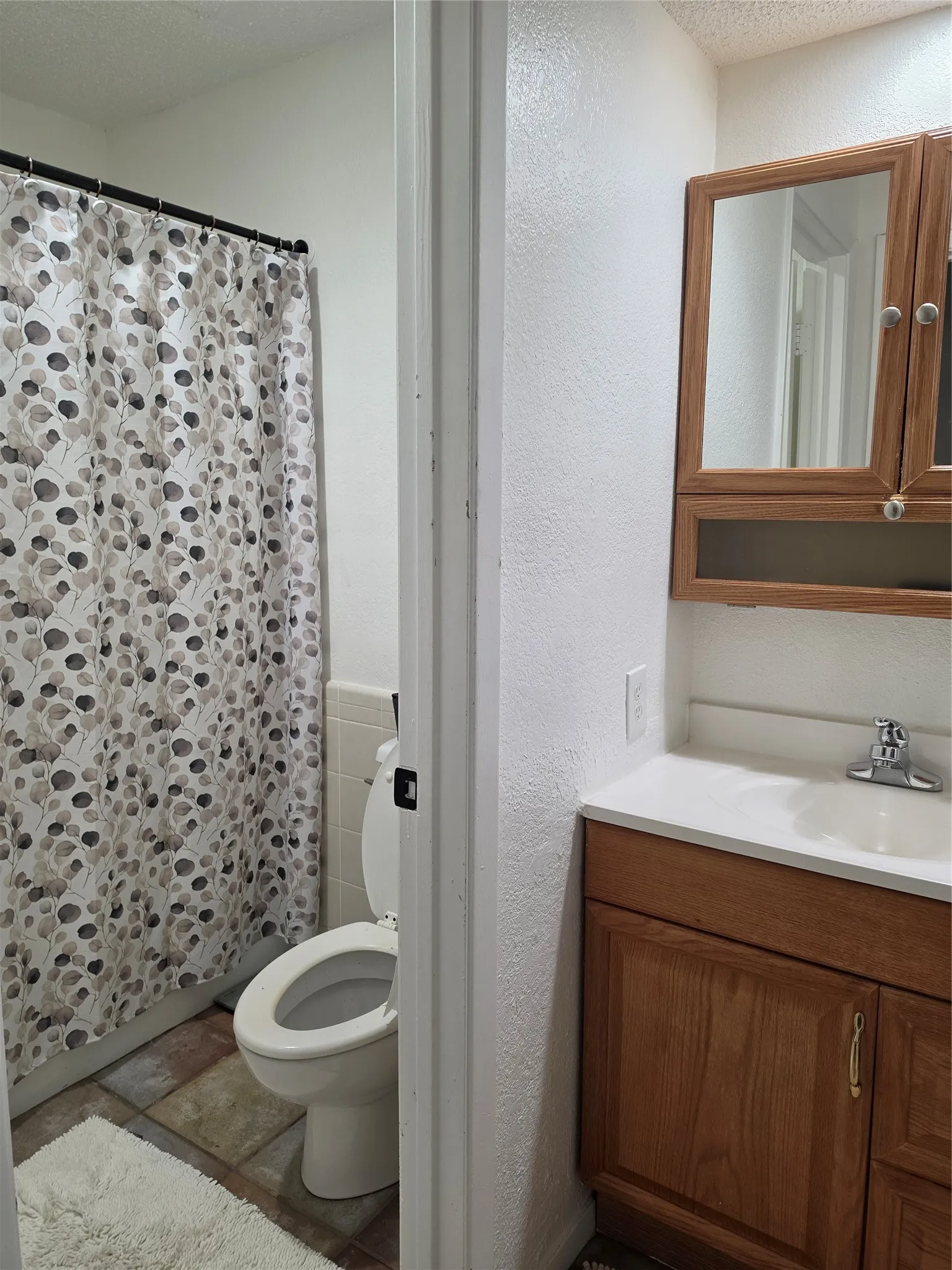 Bathroom featuring a wood-finish vanity with a white countertop and integrated sink, mirrored medicine cabinet, and a toilet