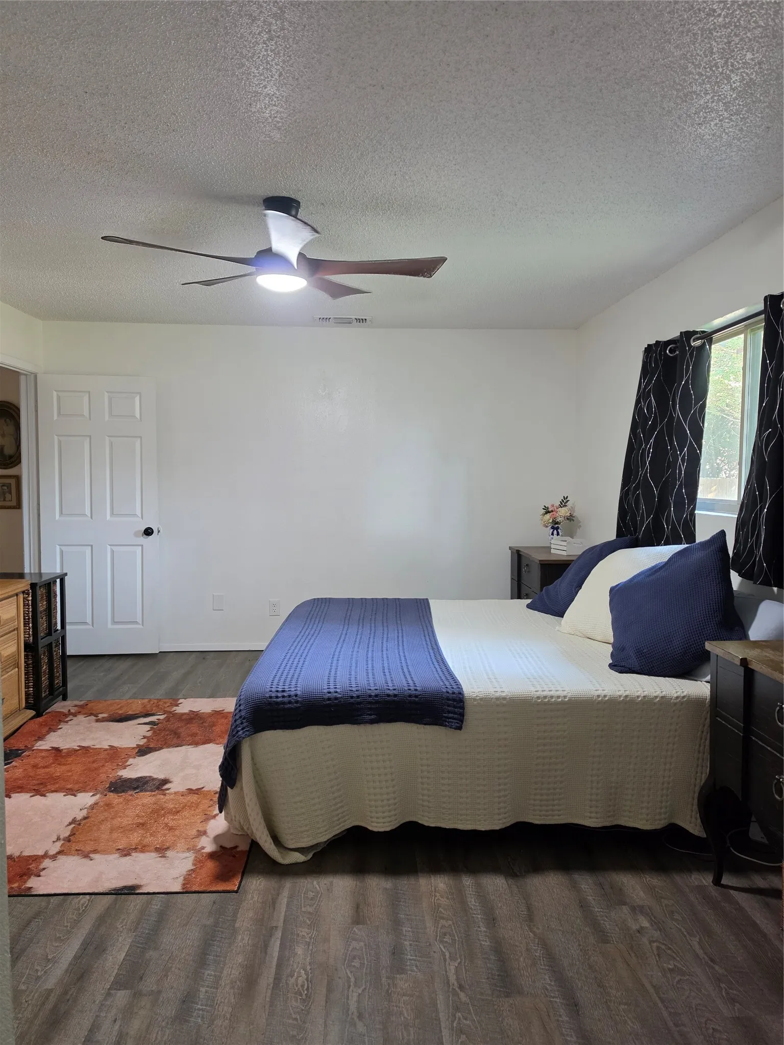 Spacious room featuring wood-finish flooring, a modern ceiling fan with integrated lighting, and multiple windows with dark drapery