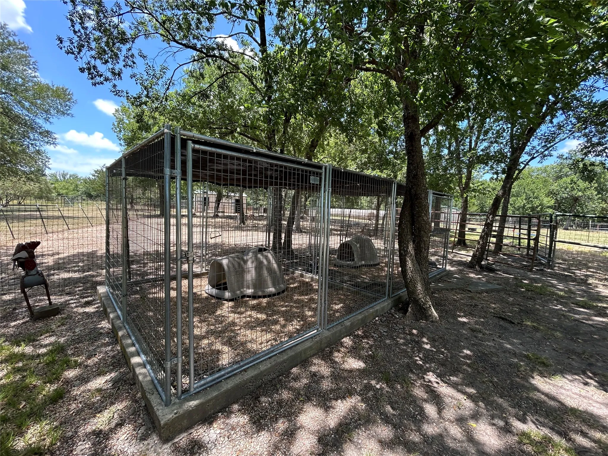 Enclosed pen structure with concrete foundation, metal fencing, and overhead shading