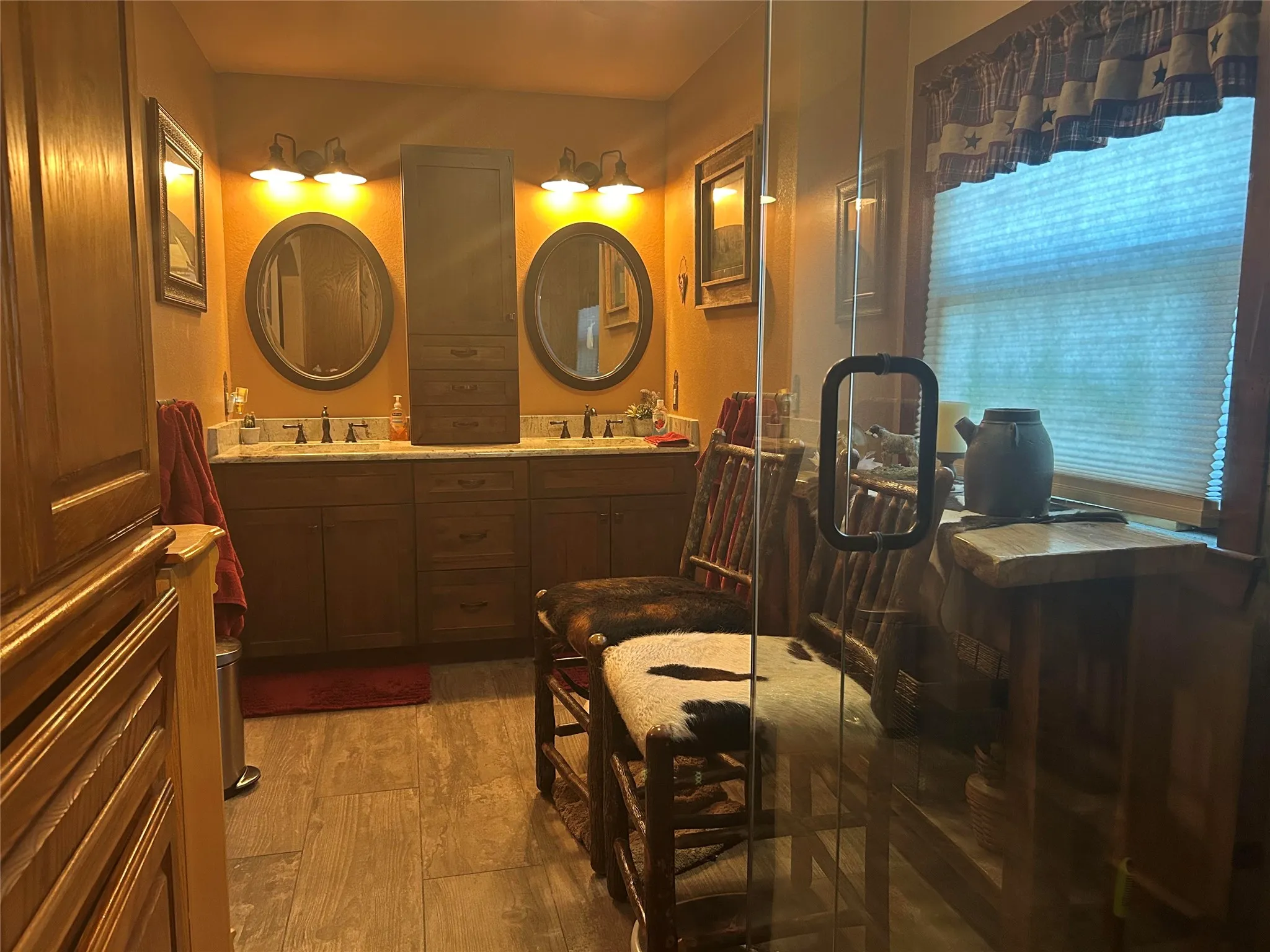 Bathroom featuring a double vanity with two oval mirrors, wall-mounted sconces, and a central tall storage cabinet