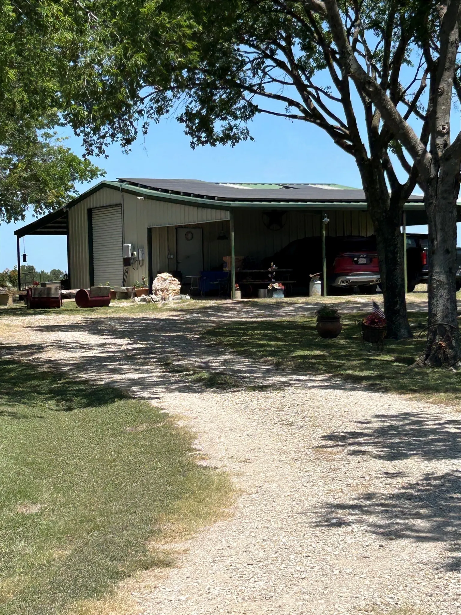 24x24 Workshp with an attached carport, gravel driveway, and surrounding green lawn