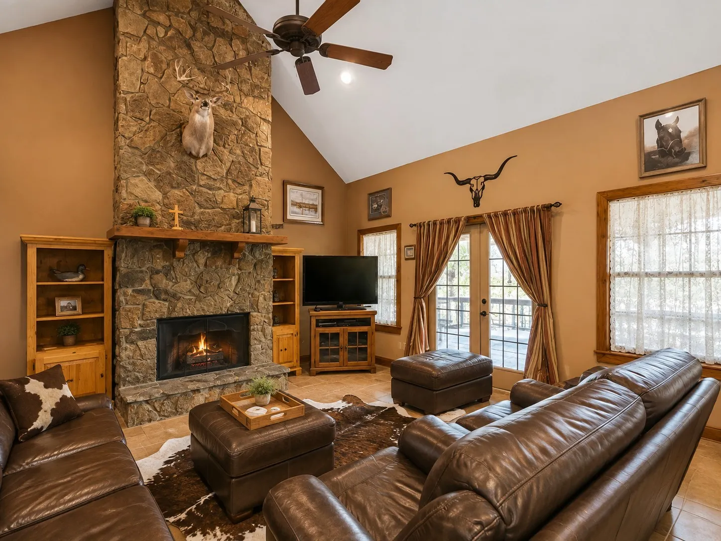 Spacious living area featuring a floor-to-ceiling stone fireplace, vaulted ceiling with a ceiling fan, and tile flooring