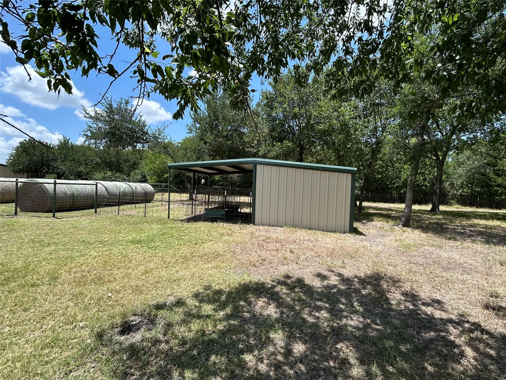 Metal-sided shed with a green trim roof, featuring an attached fenced enclosure