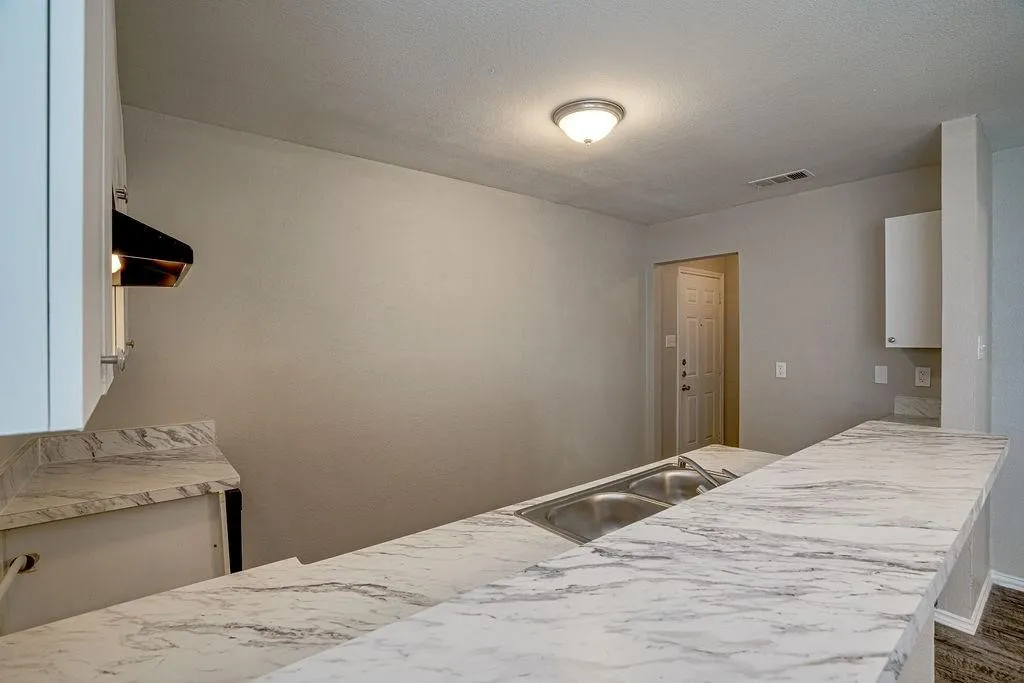 Kitchen features white cabinetry, a dual basin stainless steel sink, and a white and gray patterned countertop