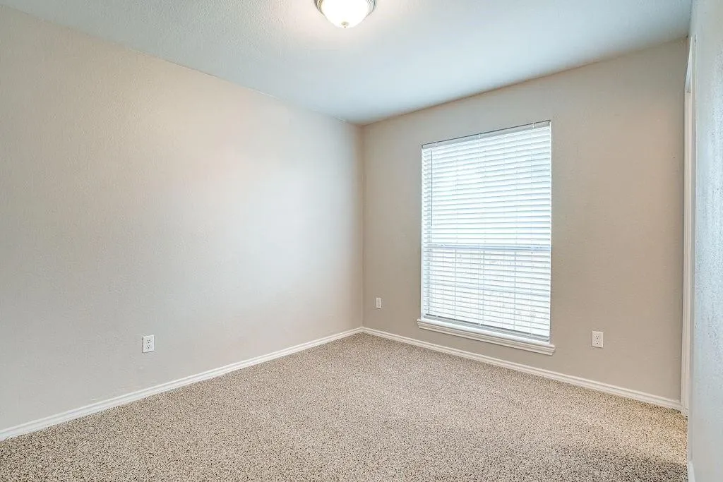 Neutral-toned interior room featuring textured walls, a single window with blinds, and a flush mount ceiling light fixture