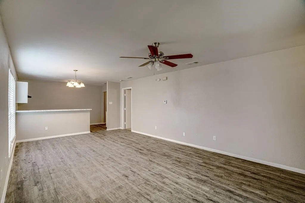 Spacious open-concept living area featuring wood-finish flooring, a ceiling fan, and neutral wall tones