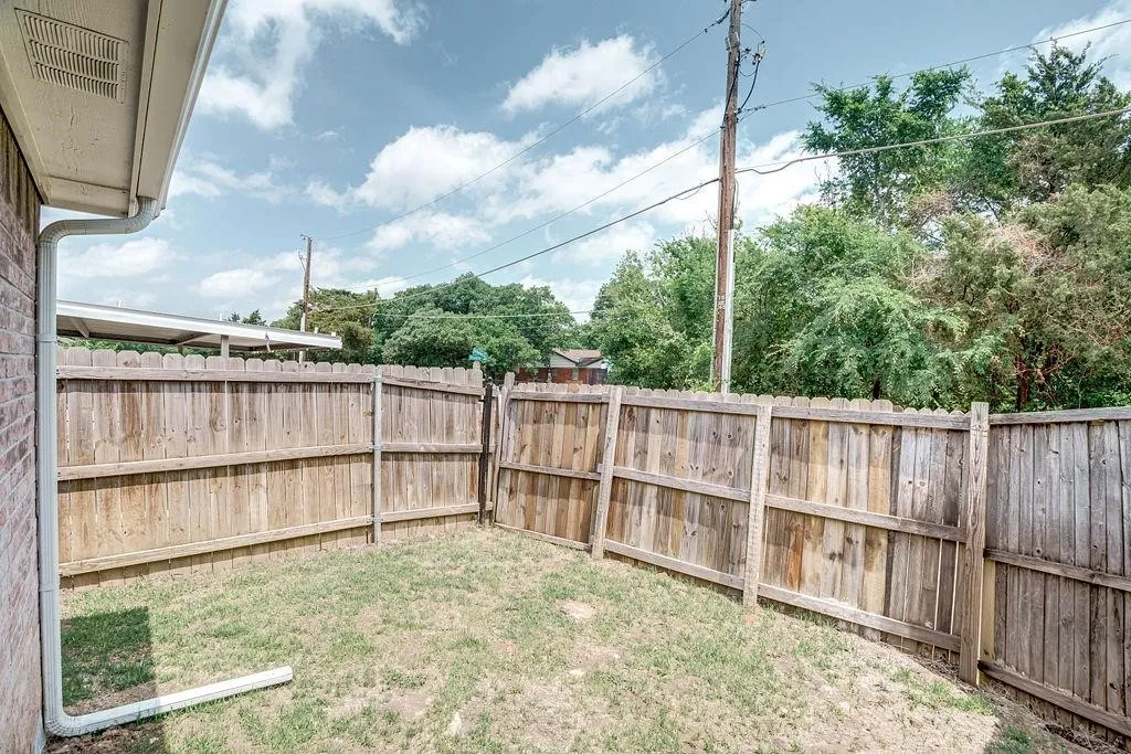 Fenced backyard featuring a wood privacy fence, grass ground cover, and a brick exterior wall with a gutter system
