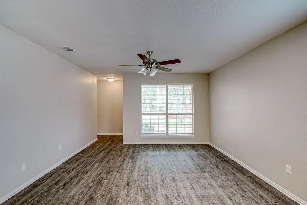 Spacious room featuring wood-finish flooring, a contemporary ceiling fan, and large windows with blinds