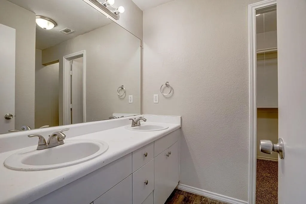 Dual vanity with integrated sinks, brushed nickel fixtures, expansive mirror, and wood-finish flooring