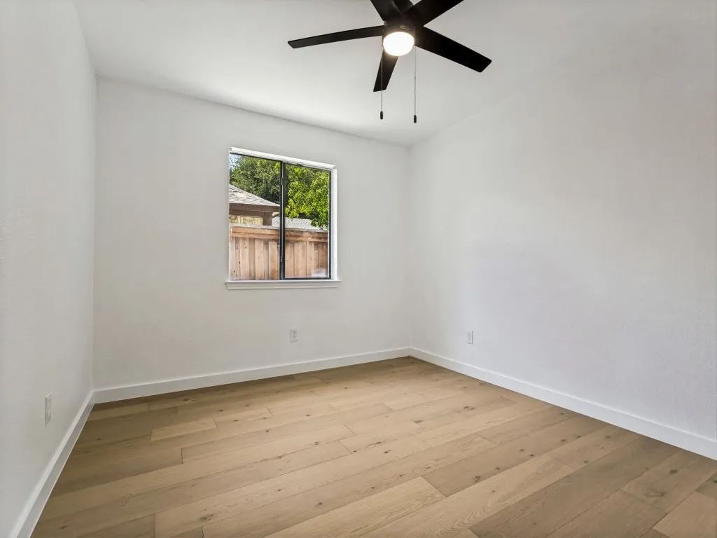 Room featuring light wood-finish flooring, white walls, and a contemporary black ceiling fan with integrated lighting
