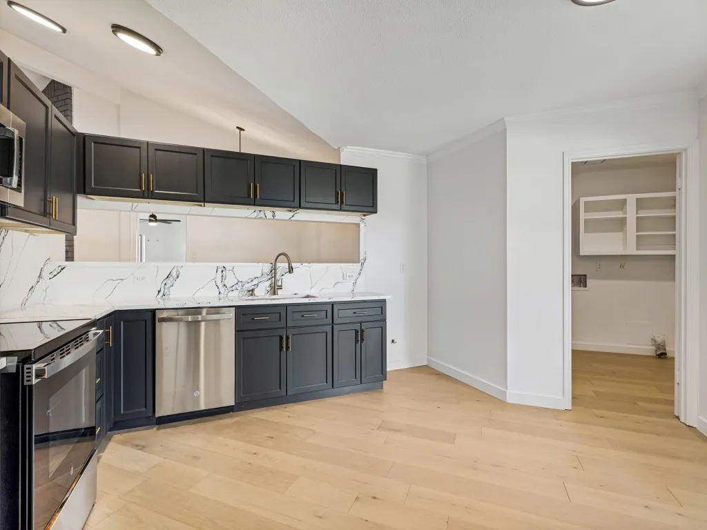 Kitchen featuring black cabinetry with gold hardware, stainless steel appliances, and wood-finish flooring