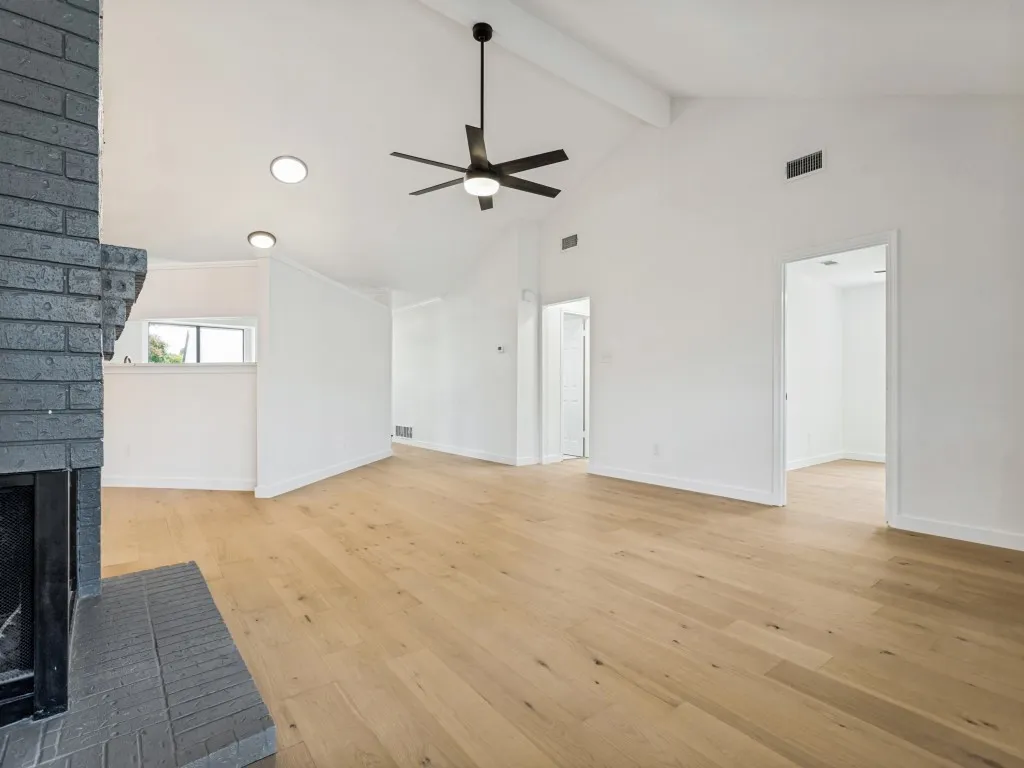 Spacious living area featuring wood-finish flooring, a vaulted ceiling, and a painted brick fireplace with a matching hearth