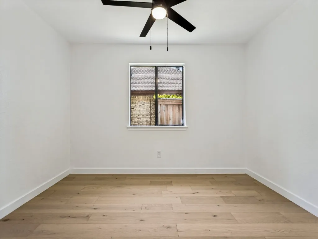 Light-filled room featuring wood-finish flooring, white baseboards, a single window, and a ceiling fan with light fixture
