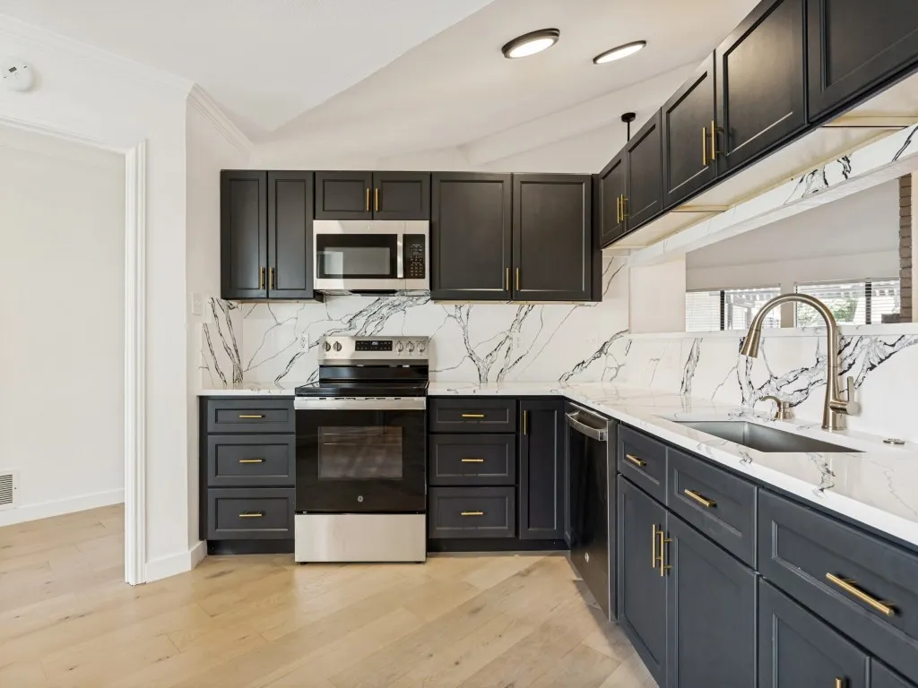 Modern kitchen featuring dark cabinetry with gold hardware, white countertops with prominent veining, a stainless steel electric range, an undermount sink with a gooseneck faucet, and wood-finish flooring