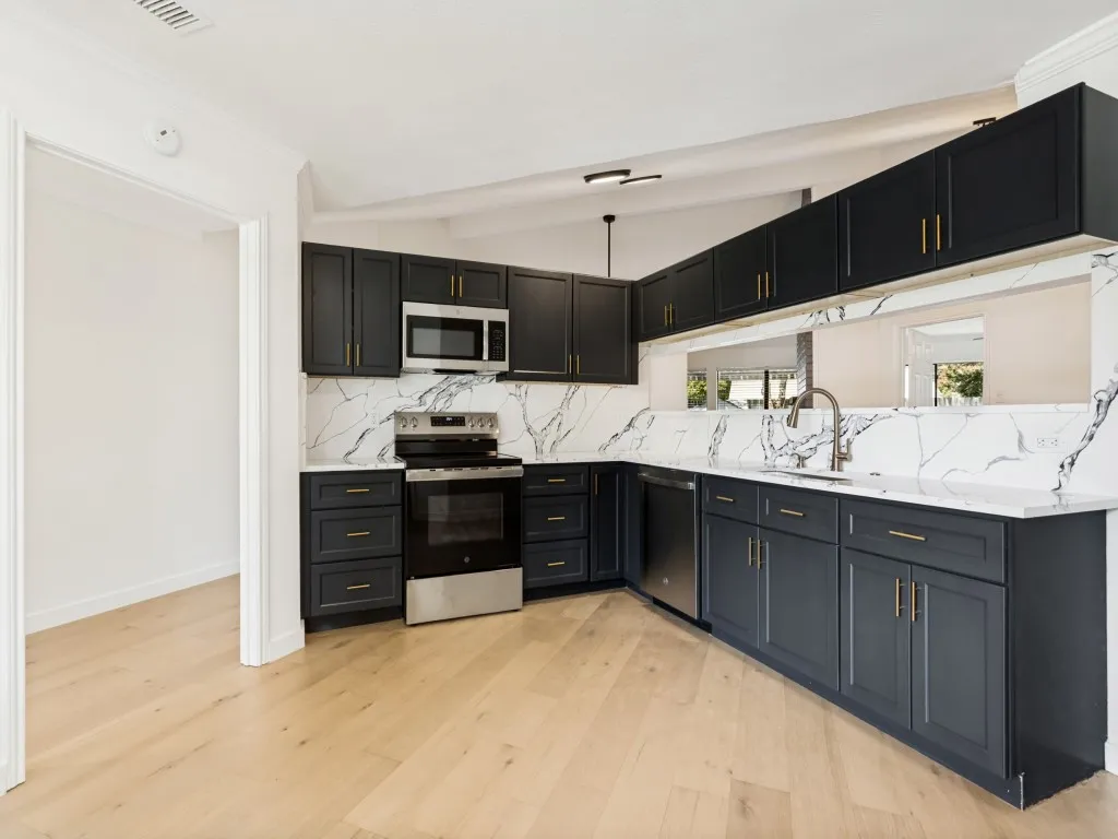 Modern kitchen featuring dark cabinetry, stainless steel appliances, light wood-finish flooring, and white countertops with a striking veined pattern