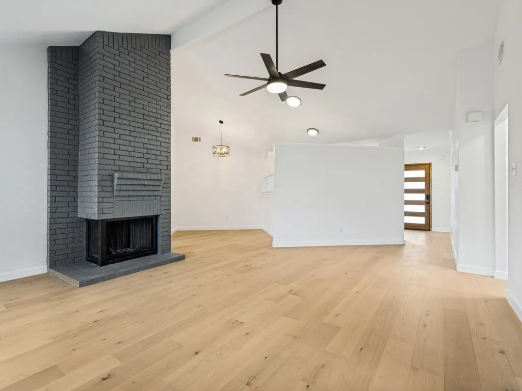 Spacious living area featuring a painted brick fireplace, vaulted ceiling, and wood-finish flooring