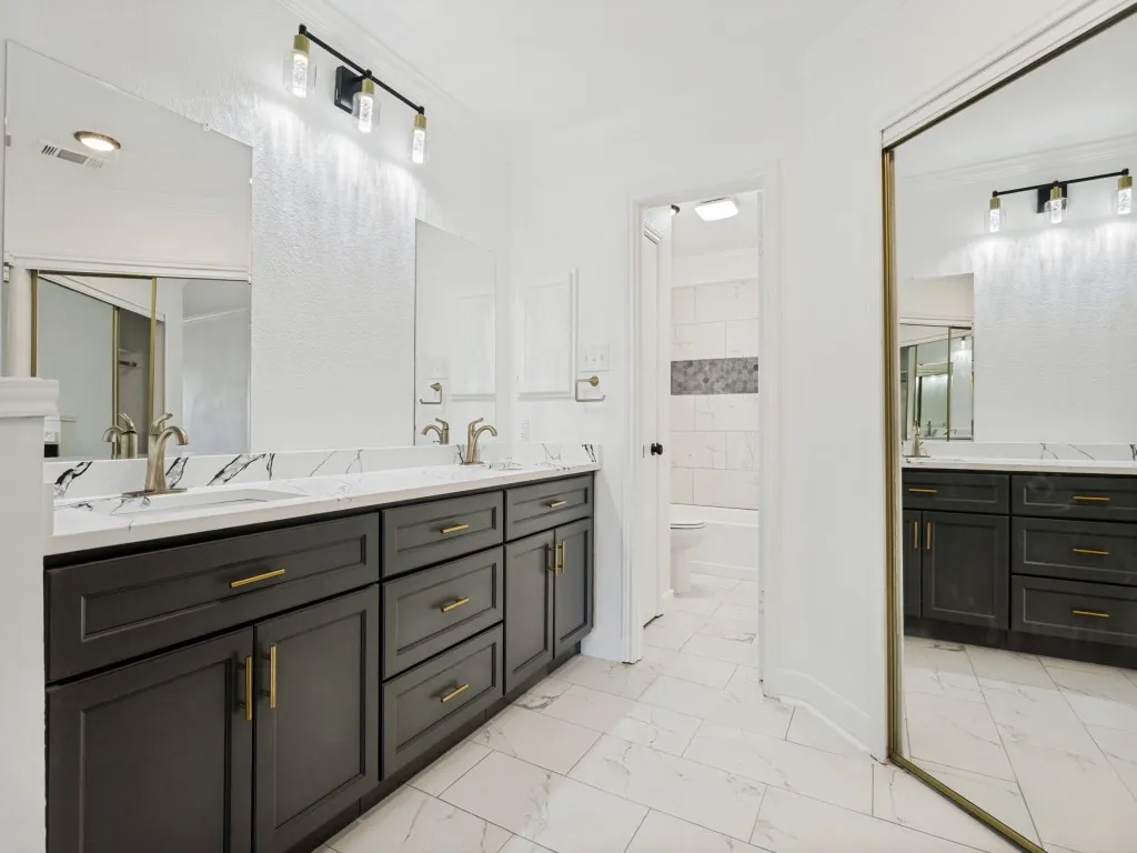 Dual vanity featuring dark cabinetry with gold-tone hardware, white countertops, and undermount sinks
