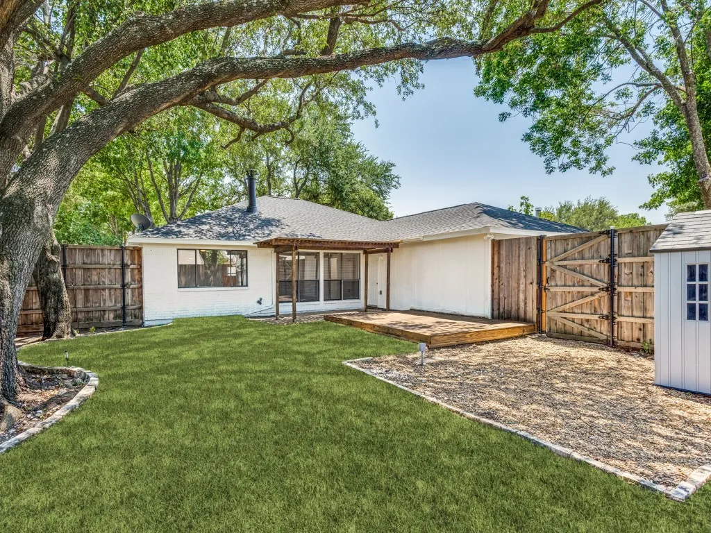 Spacious backyard featuring a wooden deck, a dedicated gravel area, a white storage shed, and a privacy fence